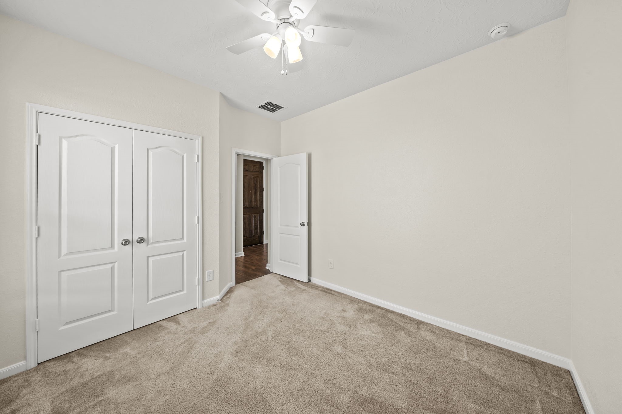 Spacious secondary bedroom featuring comfortable plush carpeting, a bright ceiling fan light, and neutral finishes.