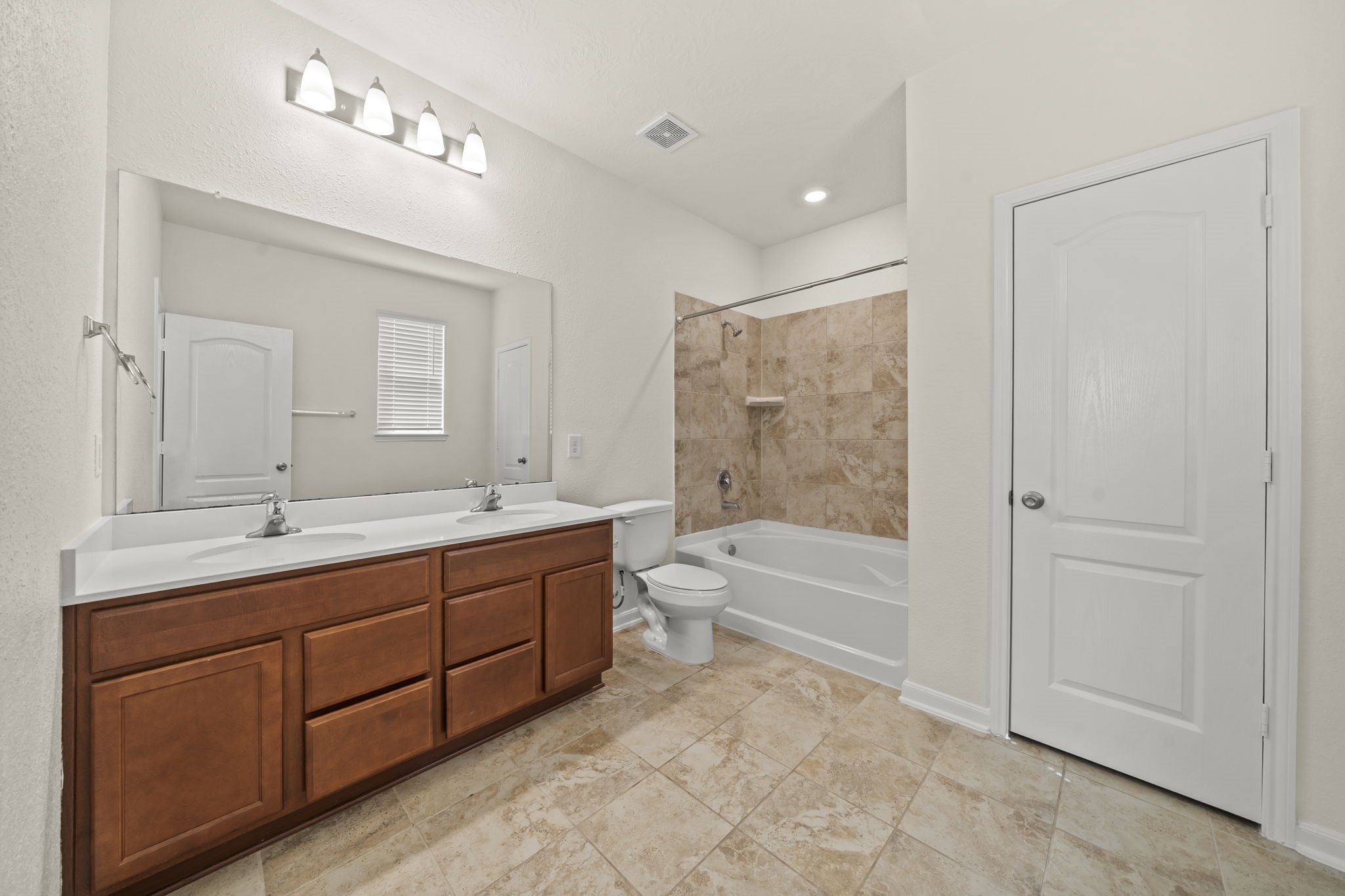 Spa-inspired primary bath featuring a dual-sink vanity with wood cabinetry, vanity mirror, and neutral tile flooring.