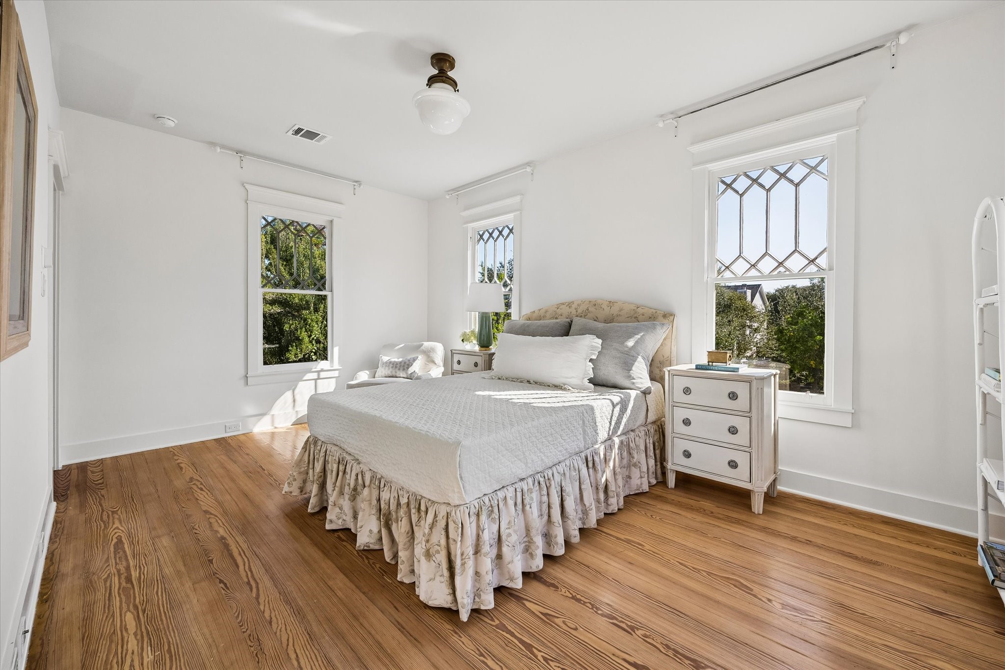 SERENE PRIMARY BEDROOM WITH RECLAIMED HARDWOOD FLOORS AND VIEWS OF THE FRONTYARD.