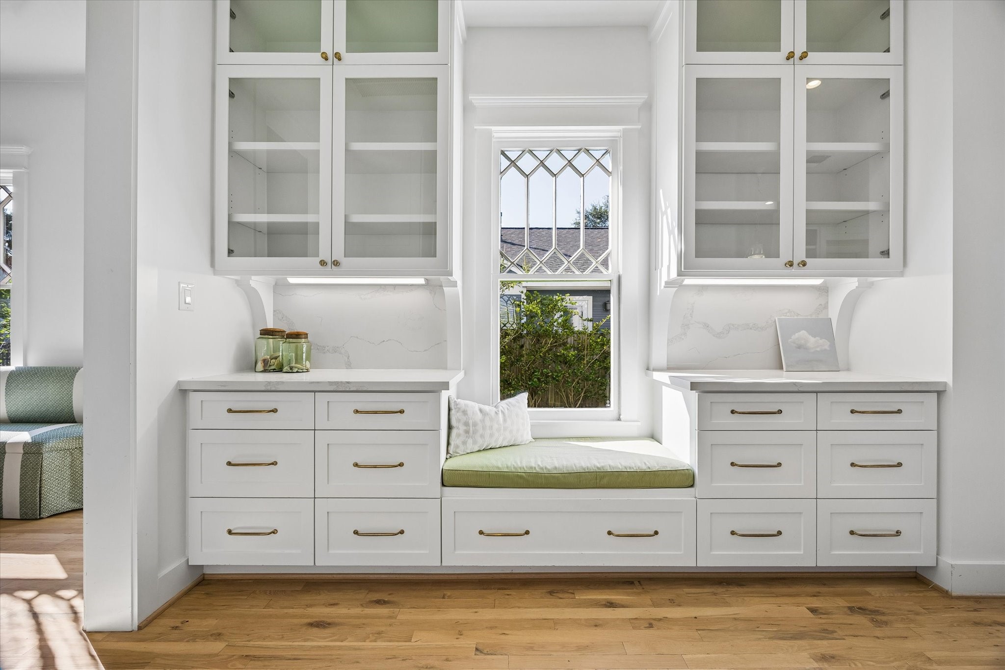 PICTURESQUE WINDOW SEAT IN THE KITCHEN, SURROUNDED BY GLASS FRONT CABINETRY AND AMPLE STORAGE SPACE BENEATH THE QUARTZ COUNTERTOPS.