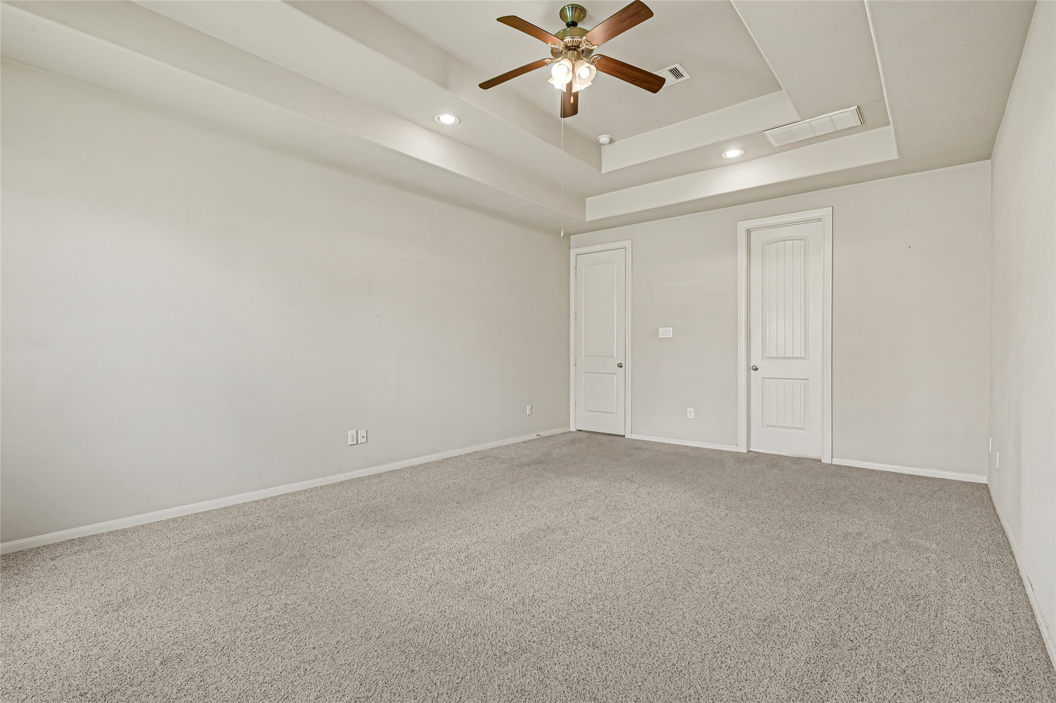 Spacious bedroom with tray ceiling, ceiling fan, neutral carpet, and abundant natural light.