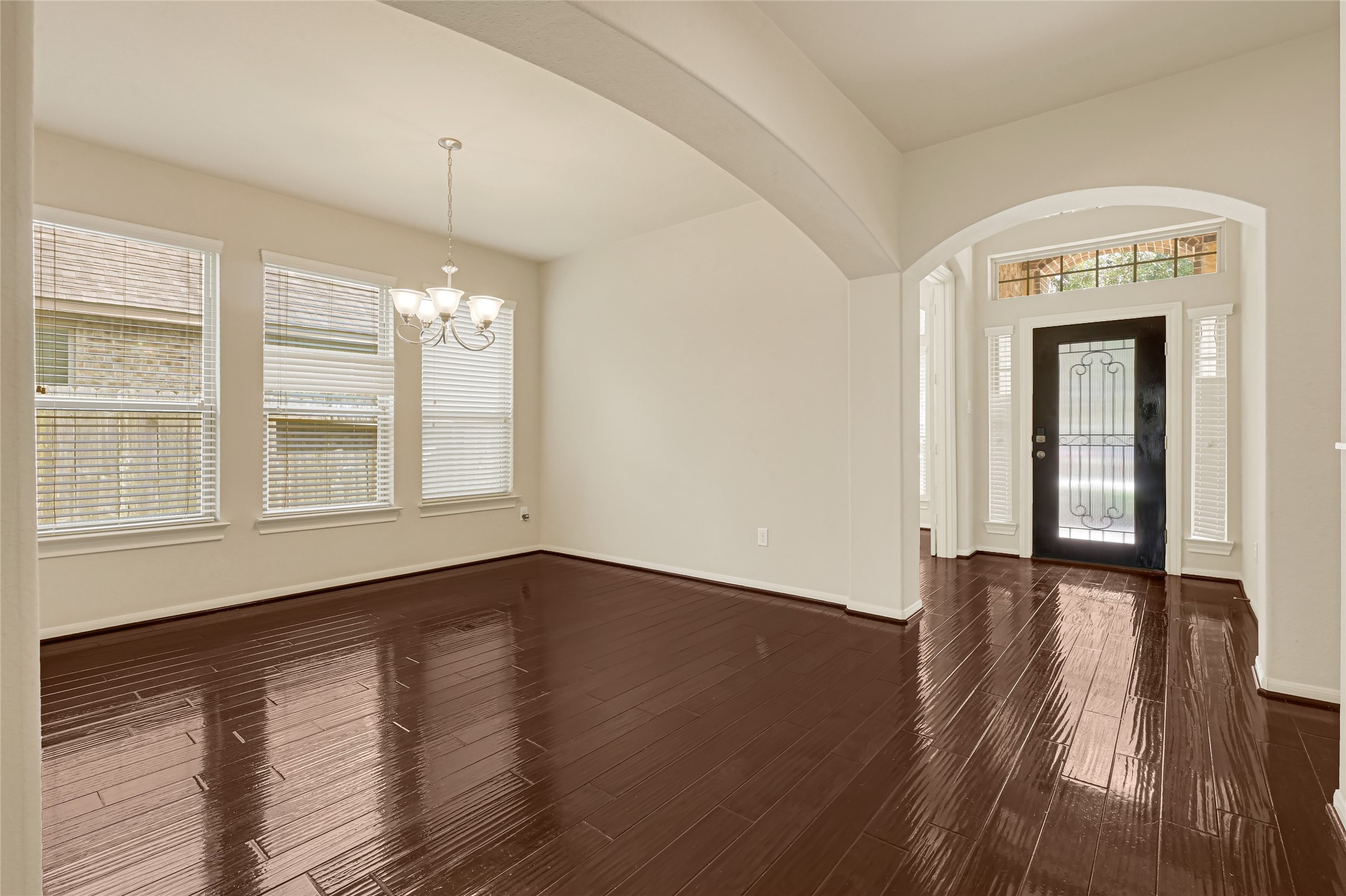 Formal dining room with hardwood flooring, crown molding, and an arched opening to the foyer.