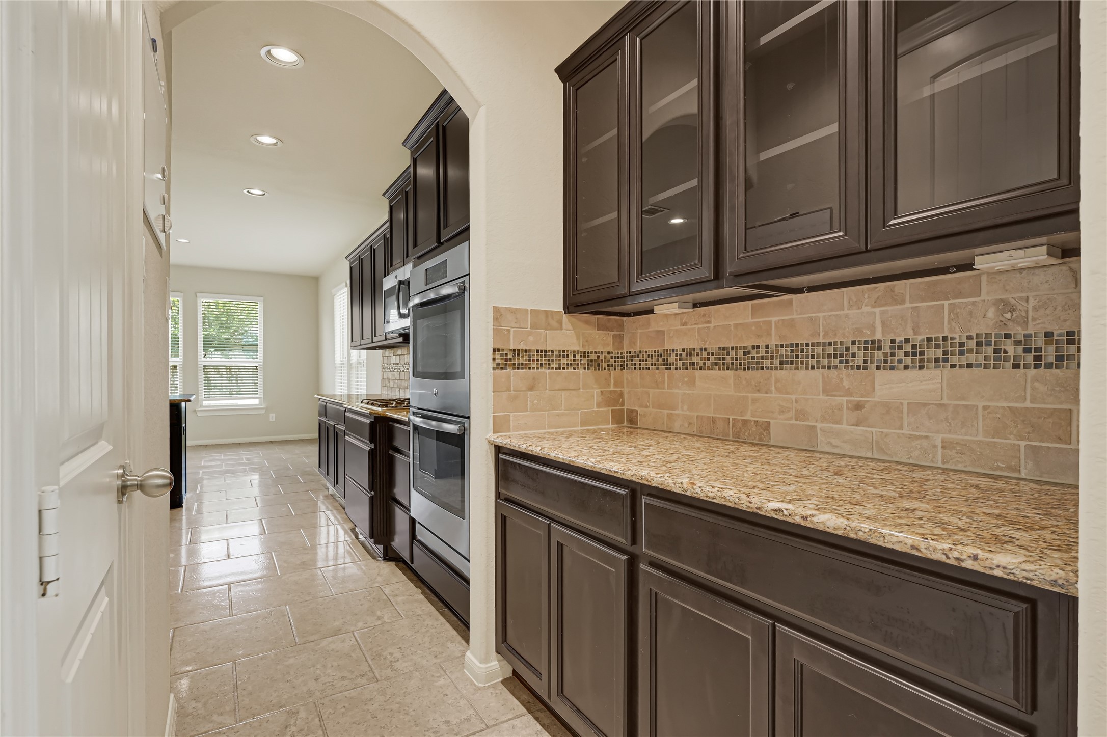 Long granite countertop with dark wood cabinetry, tiled backsplash, and generous storage.