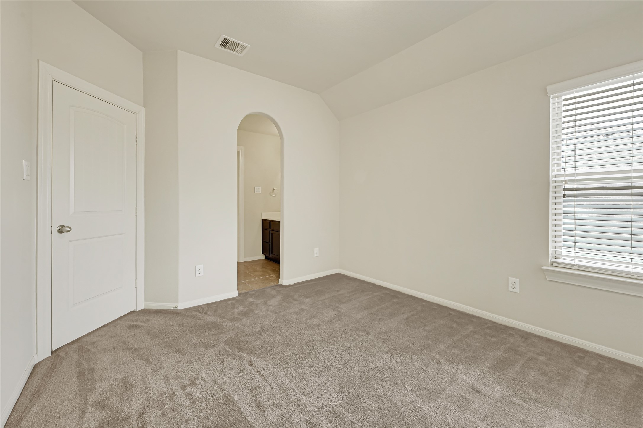 Comfortable bedroom with neutral carpet, natural light, and an arched doorway.