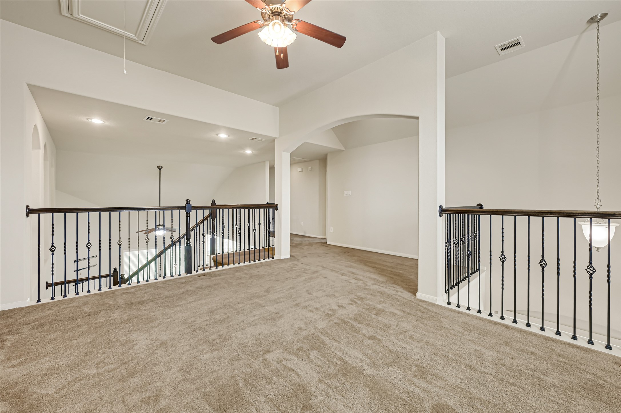 Spacious upstairs game room with neutral carpet, ceiling fan, and an open view to the lower level.