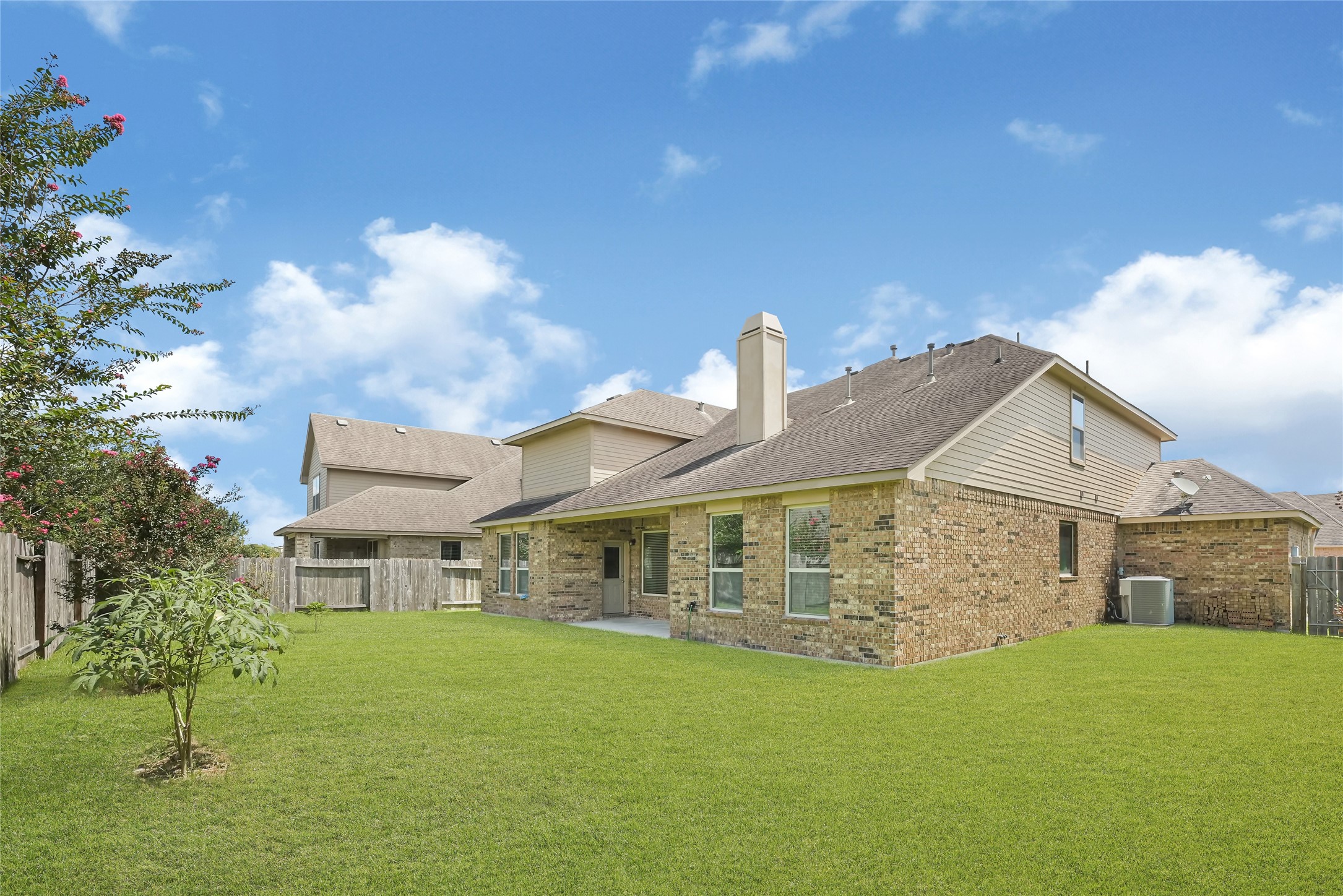 Wide backyard view showcasing the homes rear elevation, covered patio, and generous green space.