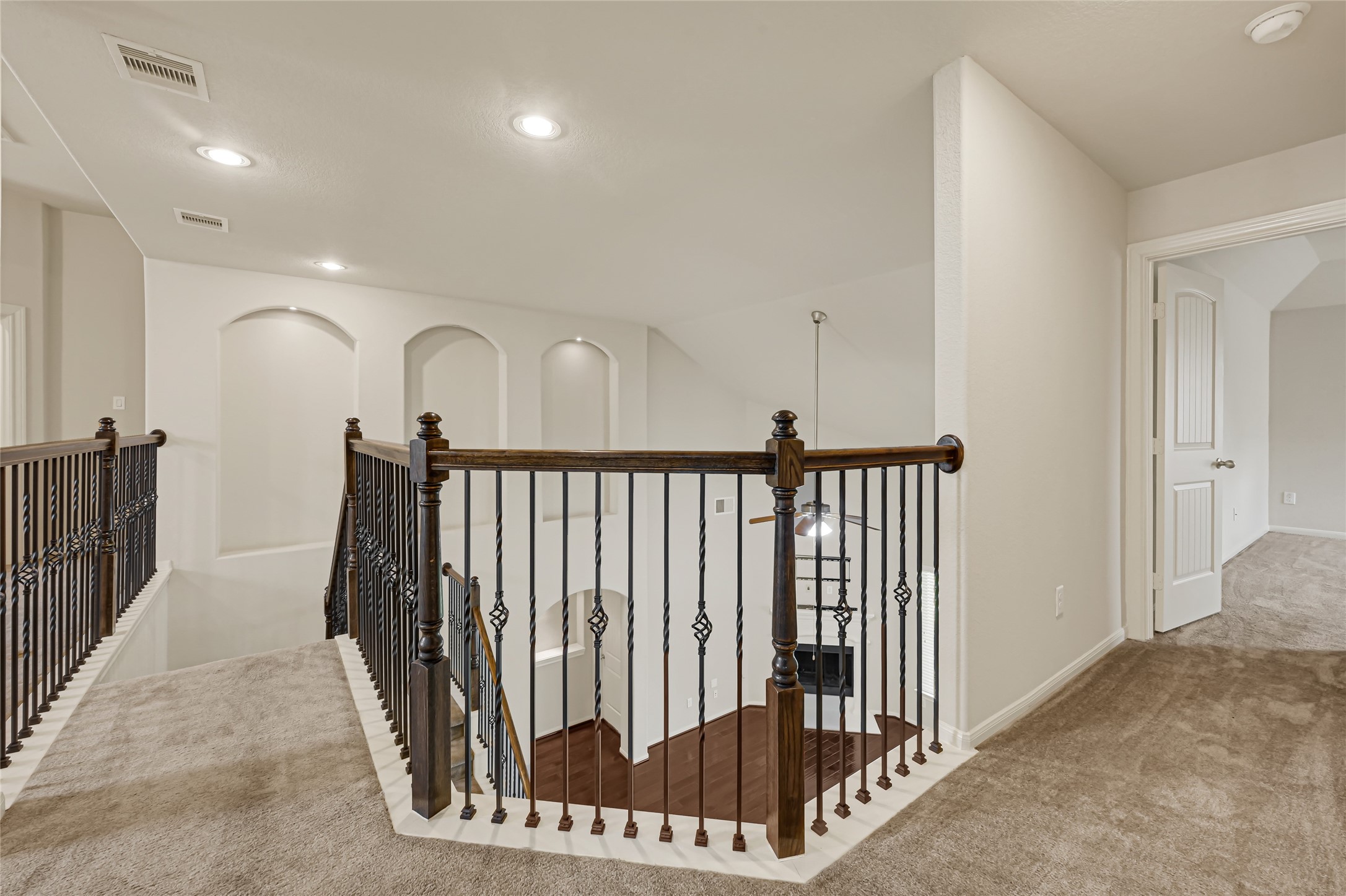 Open upstairs landing with wrought-iron railing, recessed lighting, and access to surrounding rooms.