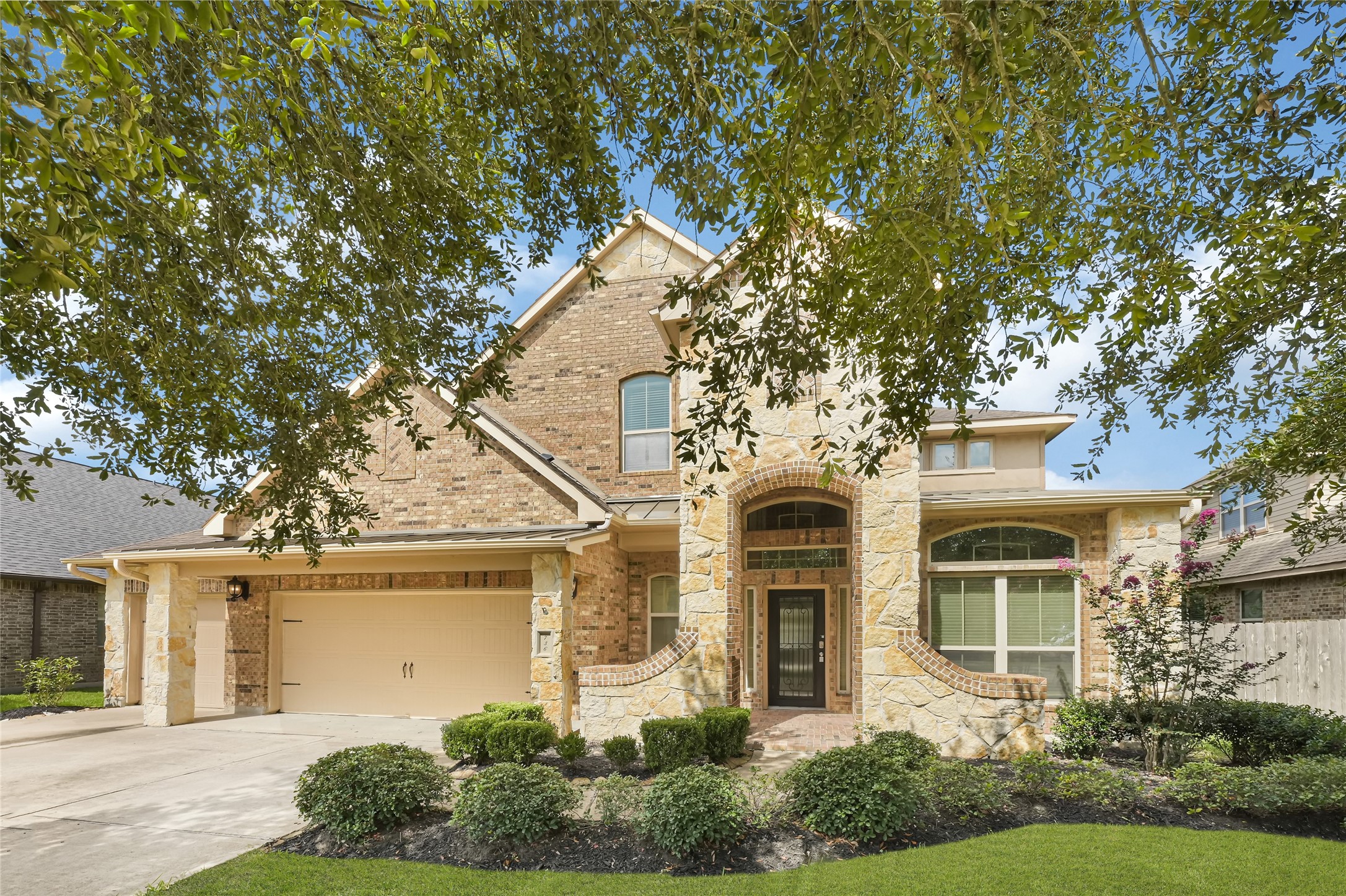 Impressive brick-and-stone exterior with a car garage, covered entry, arched architectural details, mature landscaping, and strong curb appeal.