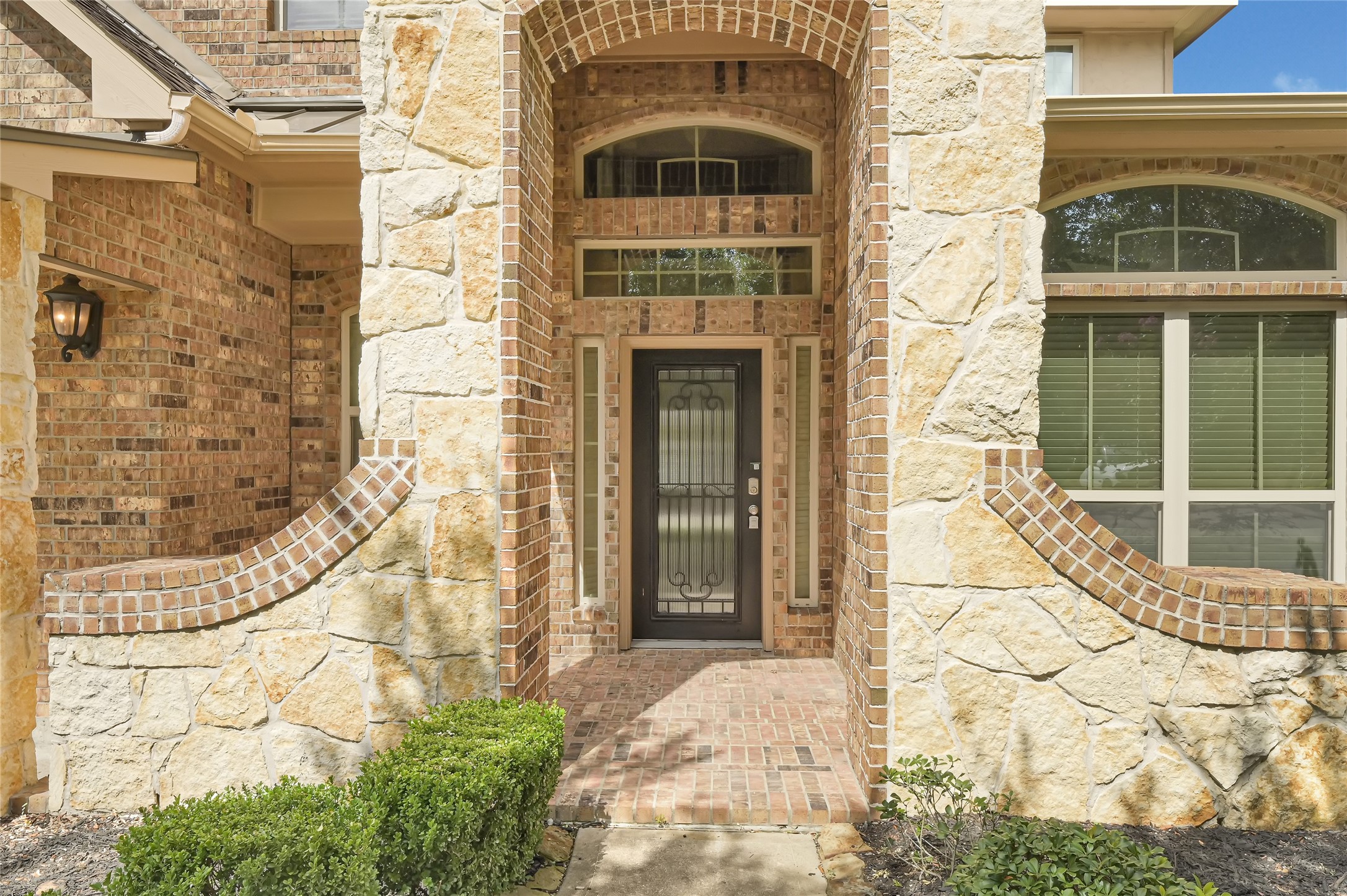 Covered front entry highlighted by stone accents, decorative glass doors, and arched architectural details.