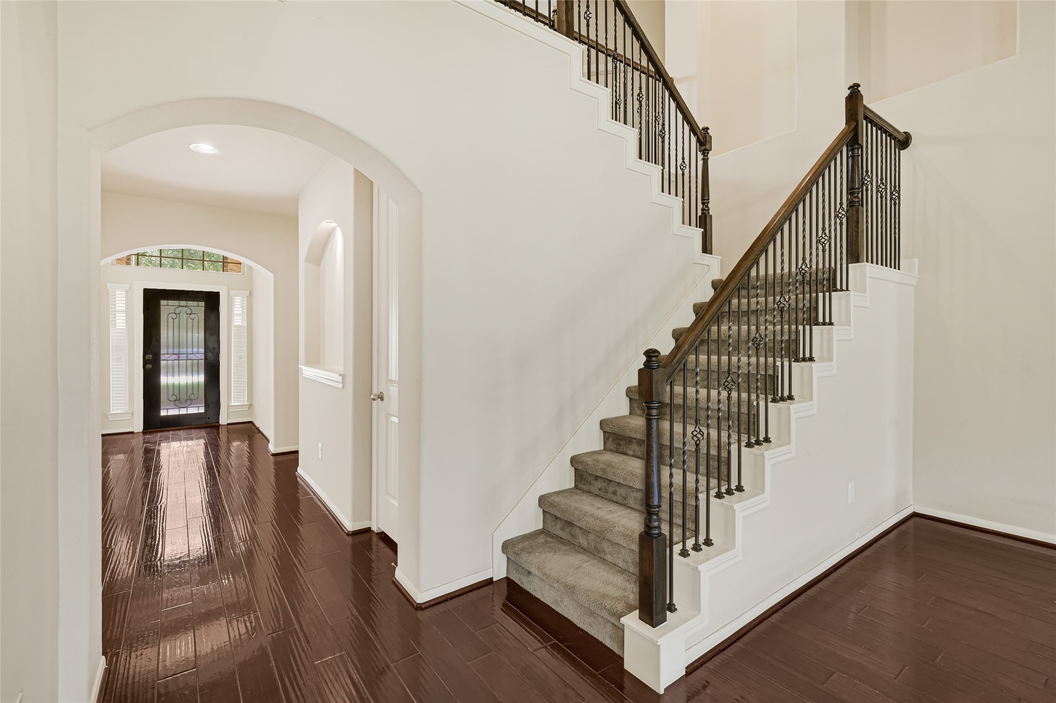 Open staircase with wrought-iron railing, hardwood flooring, and arched interior openings. Open staircase with wrought-iron railing, hardwood flooring, and arched interior openings.