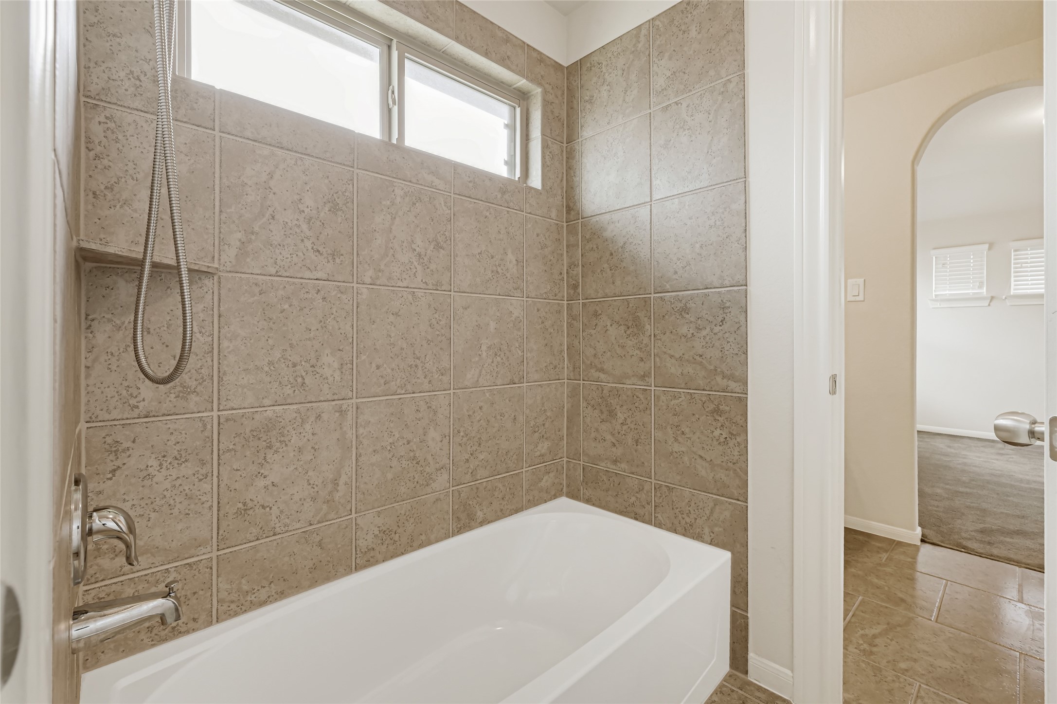 Full bathroom with a tub-and-shower combination, tiled surround, and natural light.