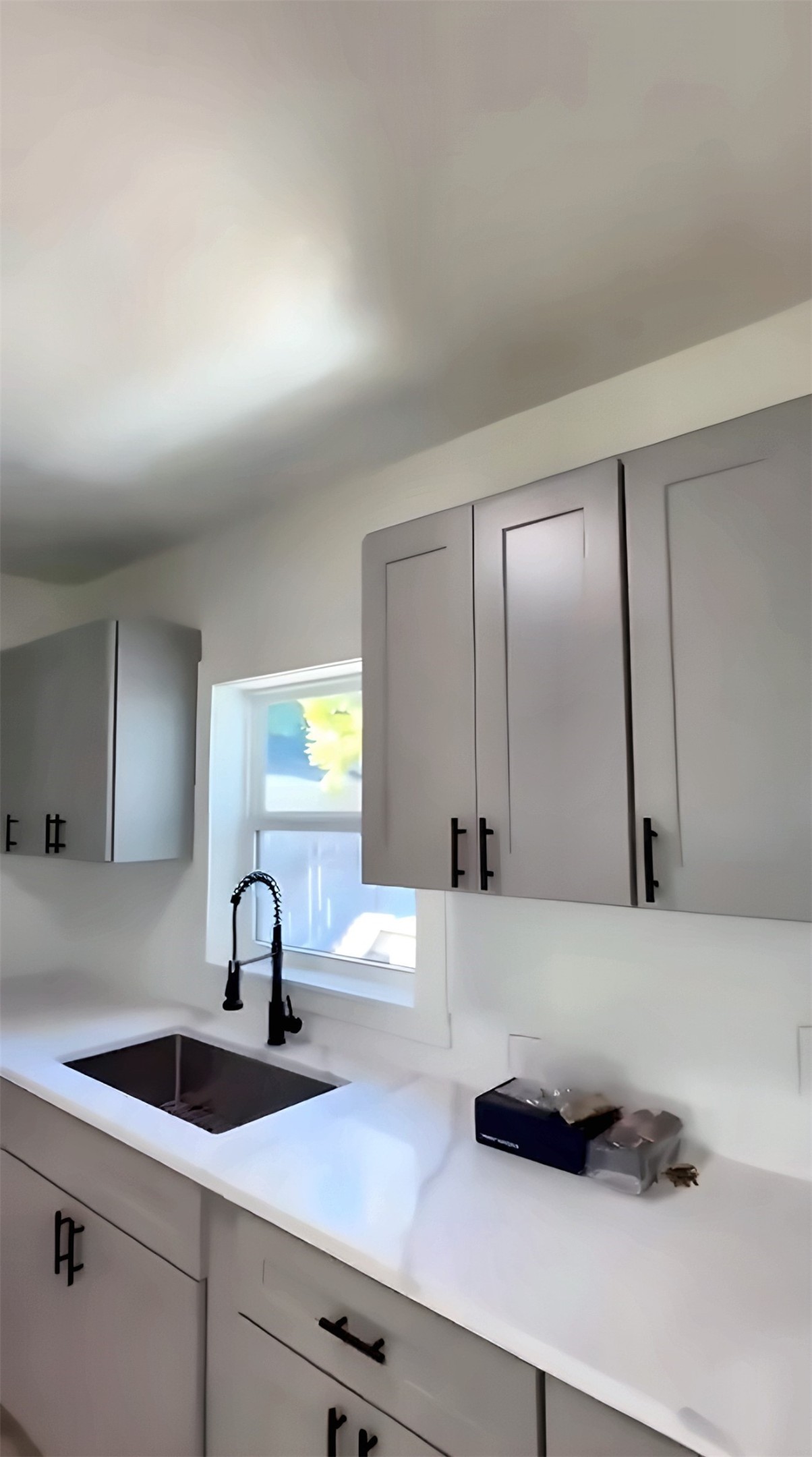 Kitchen with gray cabinets, black faucet and window