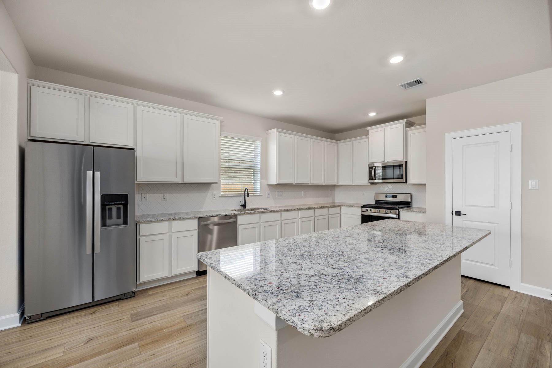 Step into this beautifully designed kitchen boasting a spacious island with a large breakfast bar overlooking the living room, a chic herringbone pattern backsplash, and modern stainless steel appliances. Perfect for entertaining and everyday living!