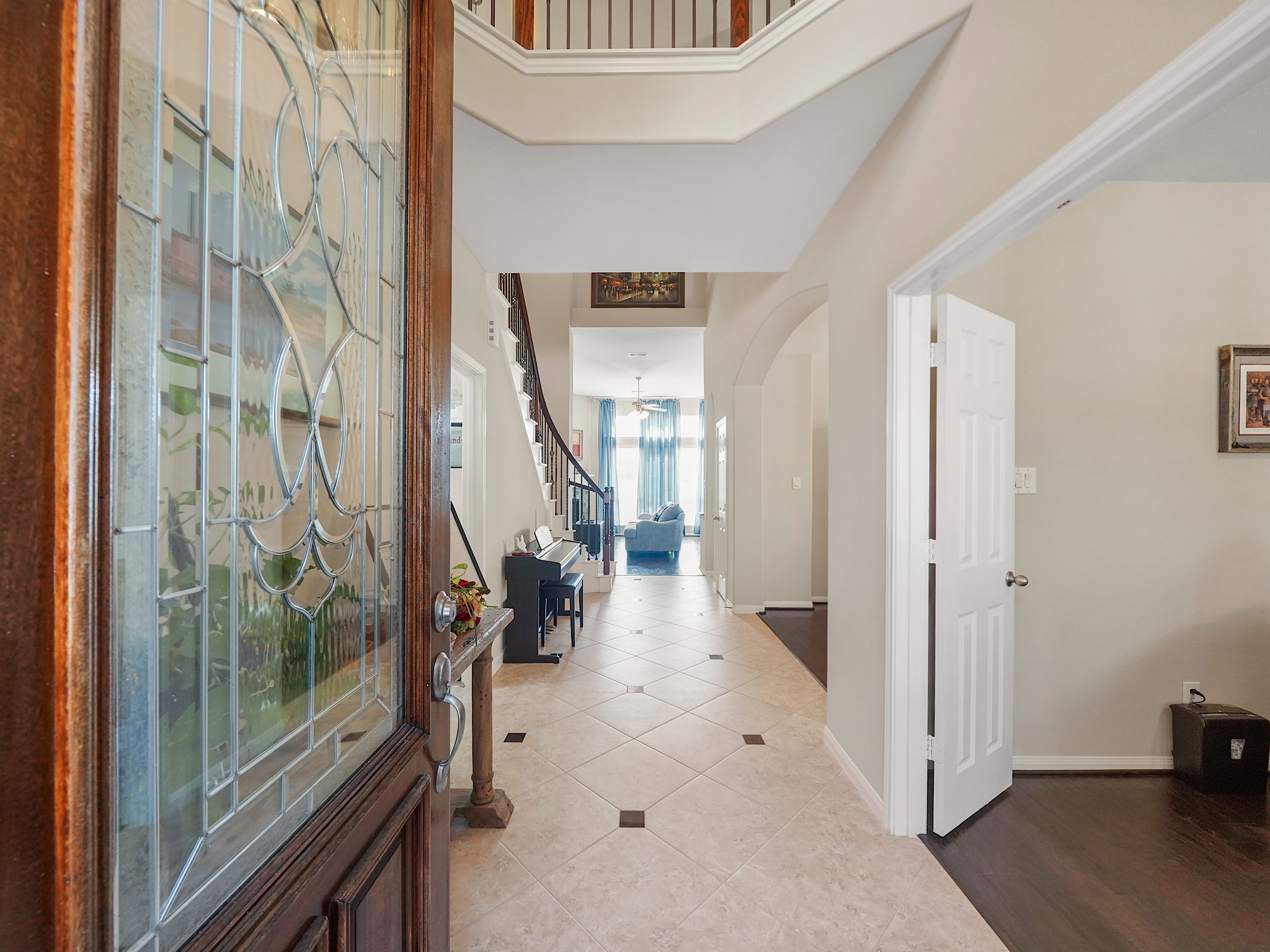 Elegant entryway with a stunning glass-paneled door, leading to a spacious hallway with tile flooring, high ceilings, and a glimpse of the inviting living area beyond.