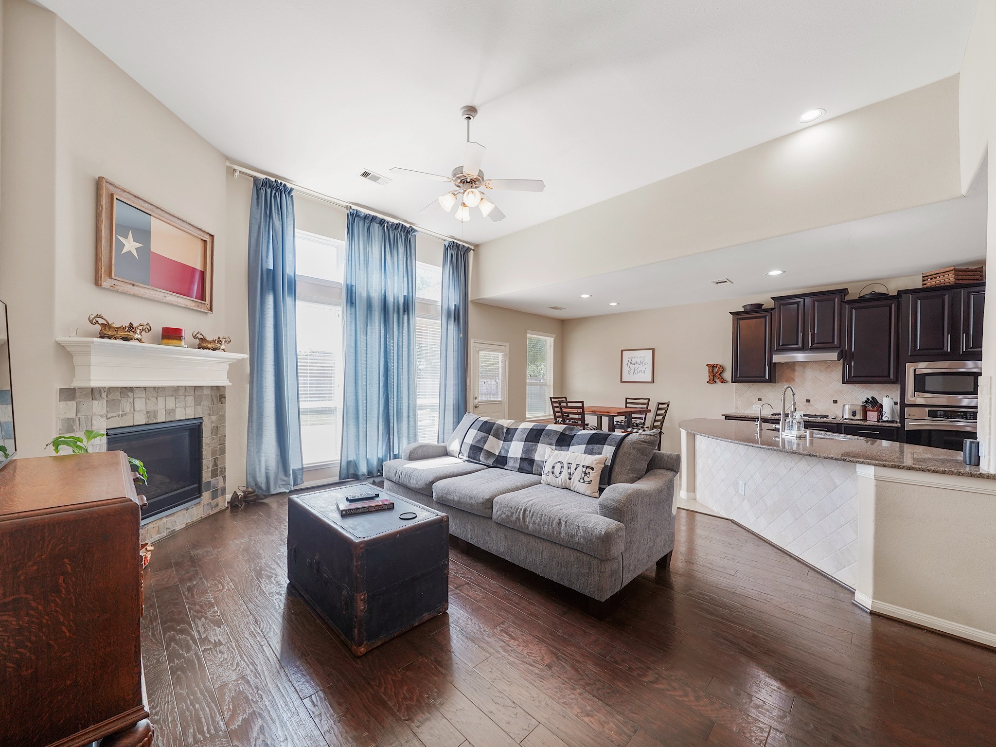Experience the inviting charm of a beautiful open living area, seamlessly connecting a cozy fireplace, modern kitchen, and ample natural light through elegant windows.