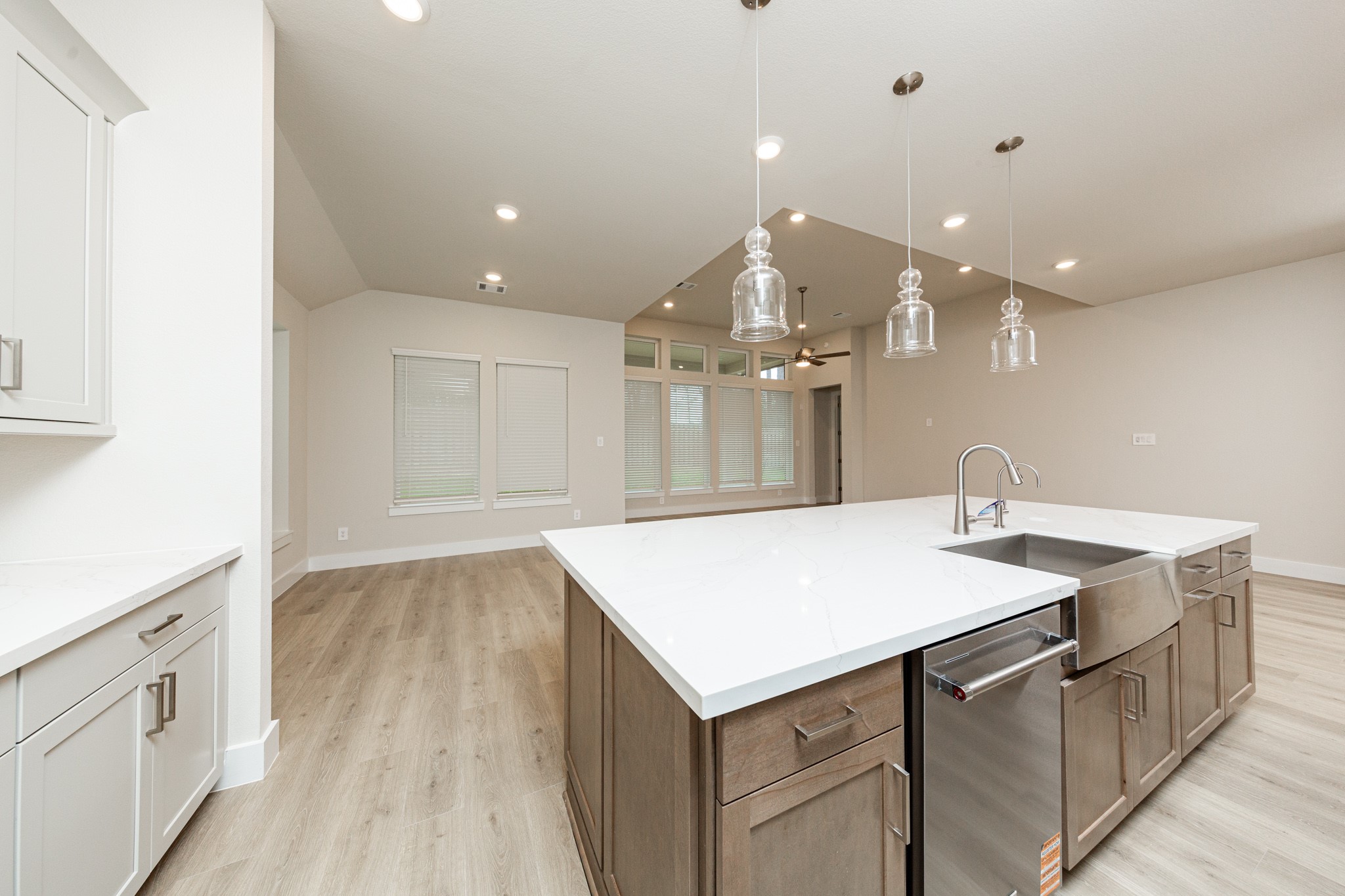 The kitchen island is a stunning centerpiece that anchors the space, while the layout provides a commanding view of the adjoining living areas and beyond. It features a seamless white quartz countertop that provides a vast workspace, complete with an integrated stainless steel apron-front farmhouse sink and a sleek, high-arc faucet.