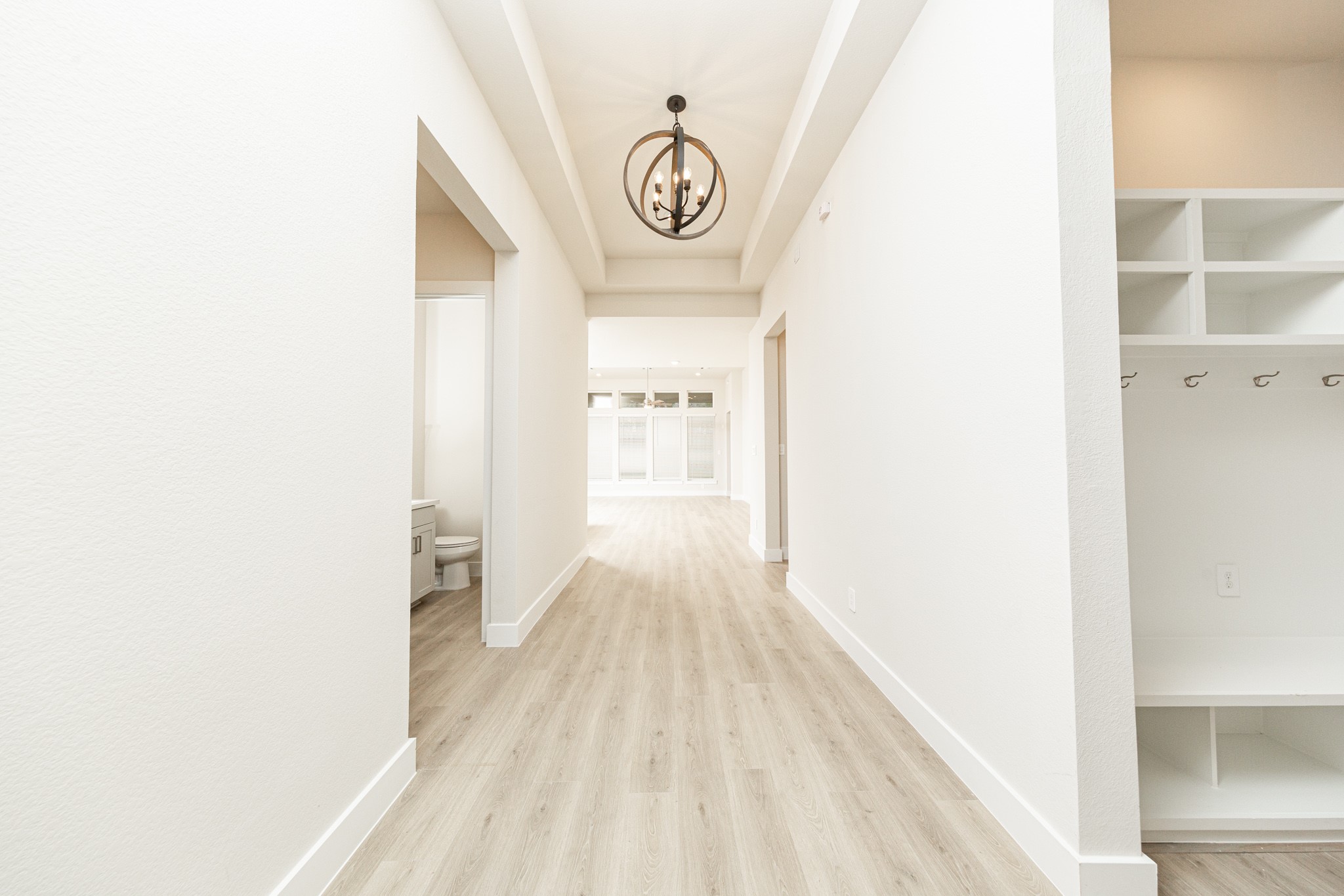 A well appointed mud room on your right is an essential feature for a busy household. The space boasts custom-built white cabinetry and shelving, providing generous storage for coats, bags, and shoes. A comfortable built-in bench offers a convenient spot to sit, while three sleek hooks keep outerwear tidy and accessible.