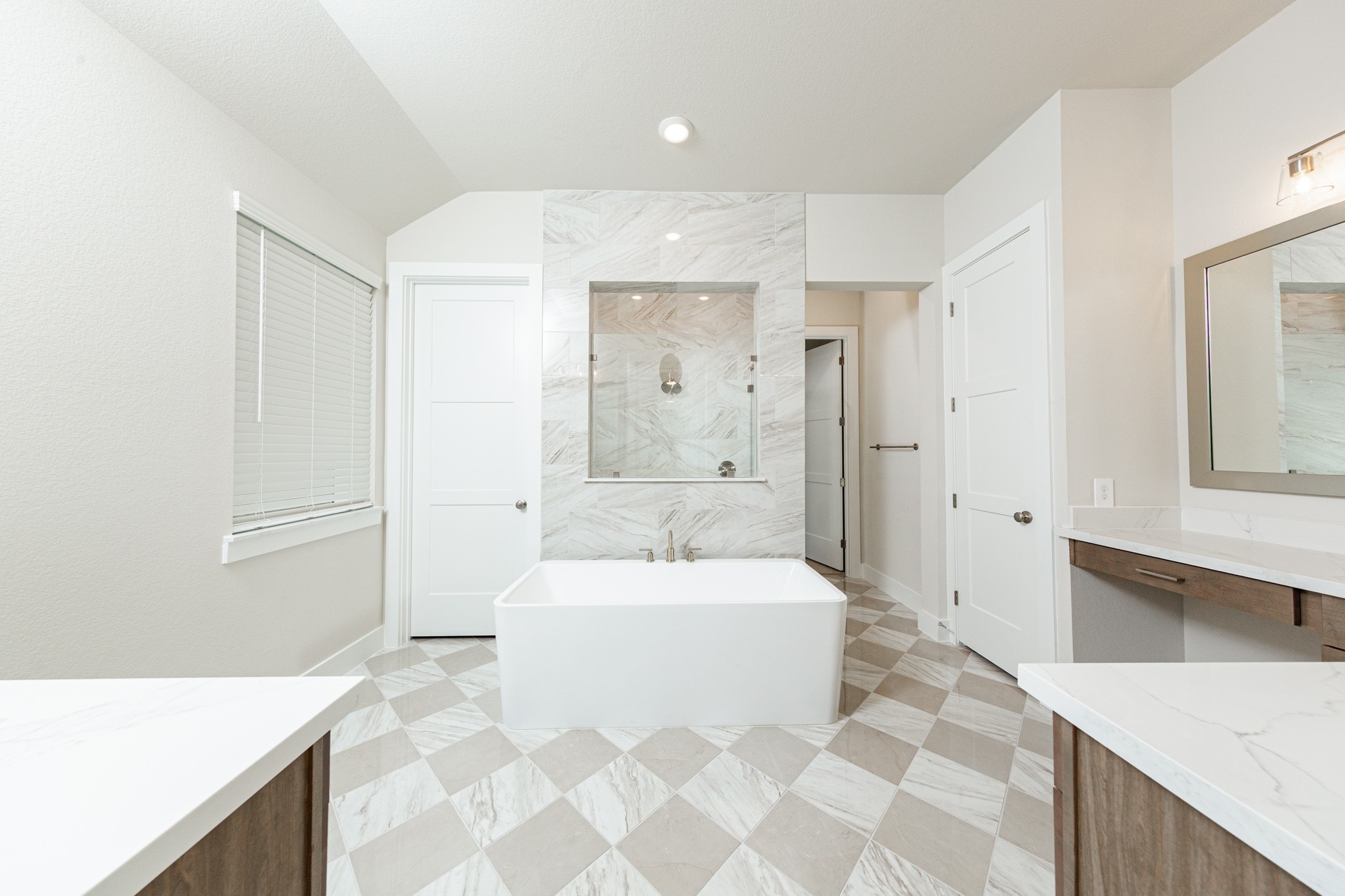 The centerpiece of this contemporary primary bath is the deep, freestanding bathtub with gorgeous marble tile offering an ideal spot for relaxation with a unique view into the walk-in shower. The flooring features large square tiles set in a timeless diagonal, checkerboard pattern, adding visual interest and depth to the space.