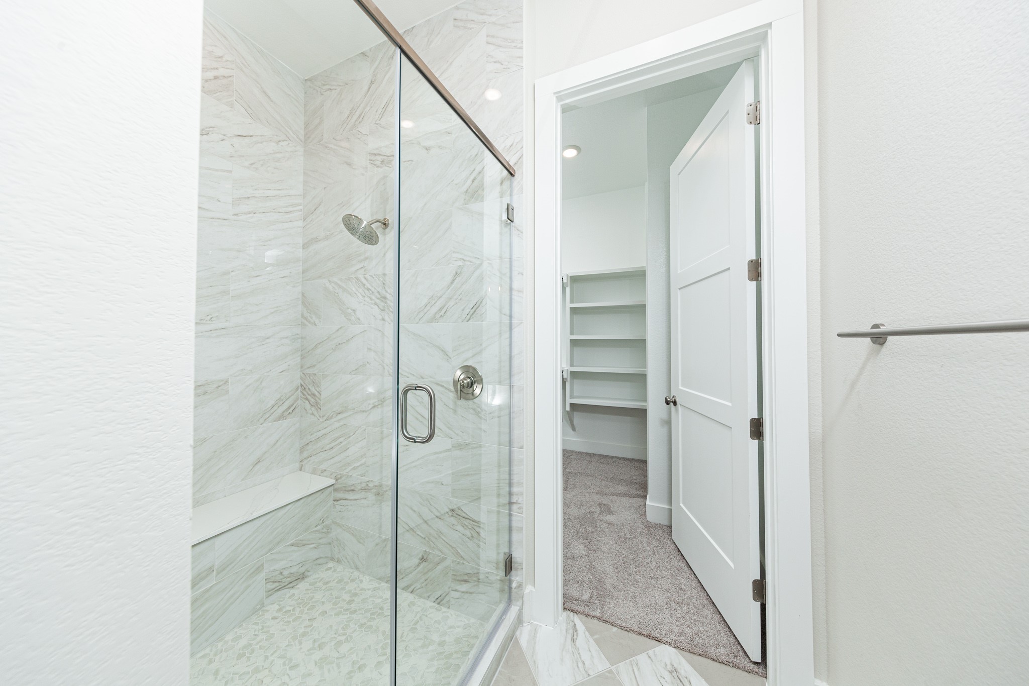 The walk-in shower includes a convenient, integrated white bench, offering comfort and a high-end, custom appearance.