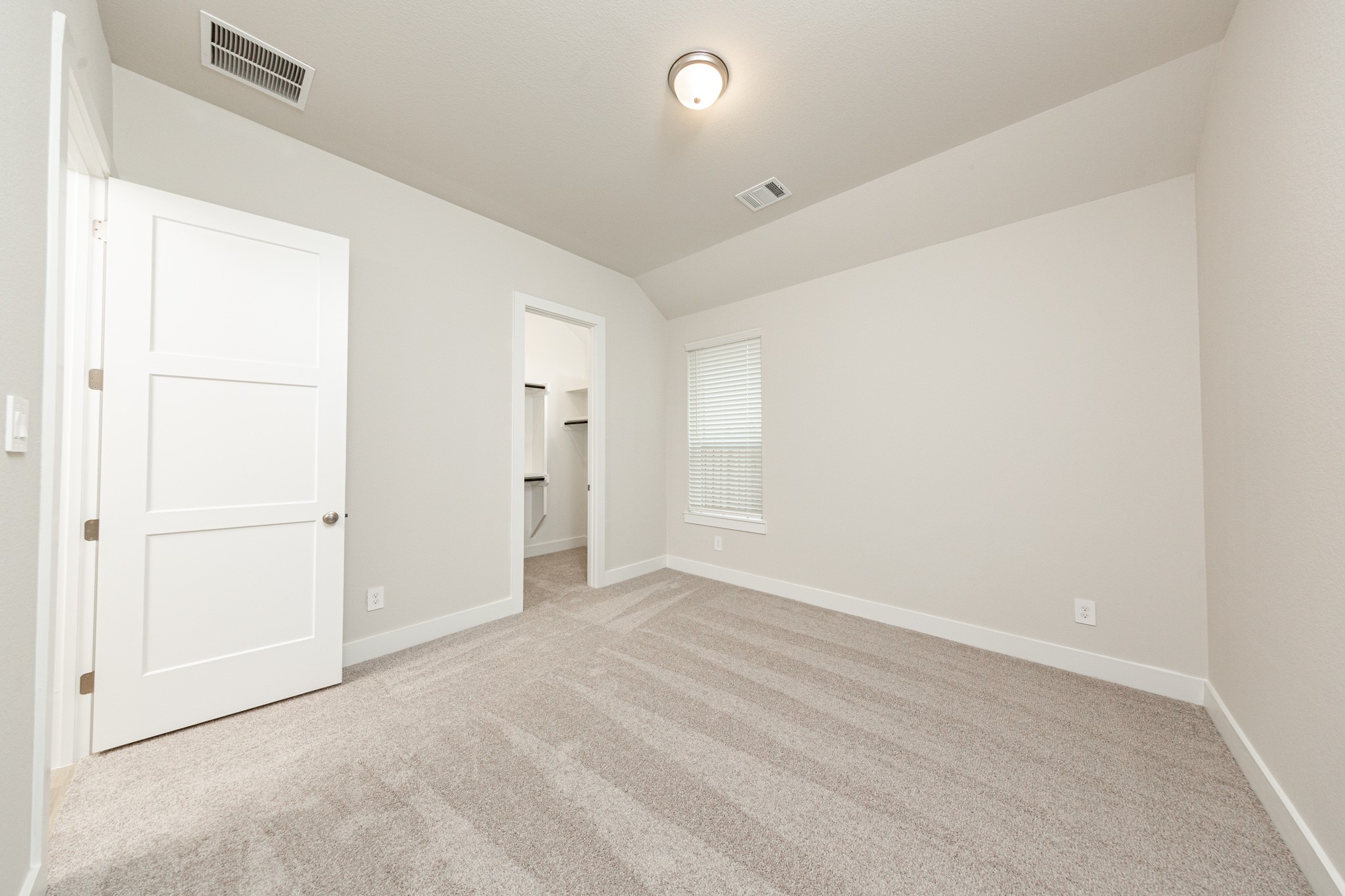 This inviting secondary bedroom combines comfort and modern elegance, featuring sloped ceiling, plush carpeting, a neutral color palette, abundant natural light streaming through a large window, and a walk-in closet.