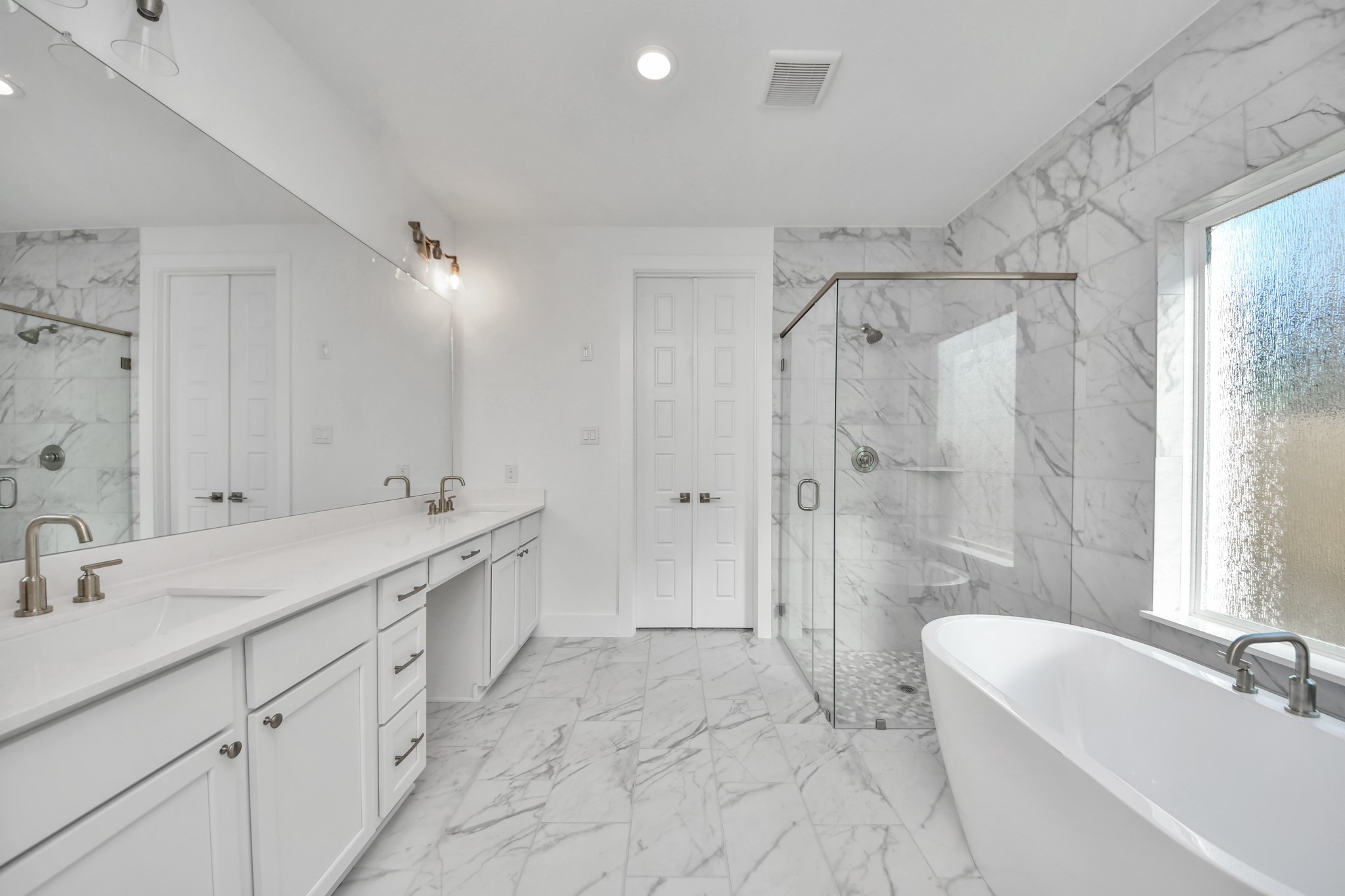 Elevate your daily routine at the elegant vanity, now equipped with double sinks, light countertops, modern hardware, and beautiful recessed lights.