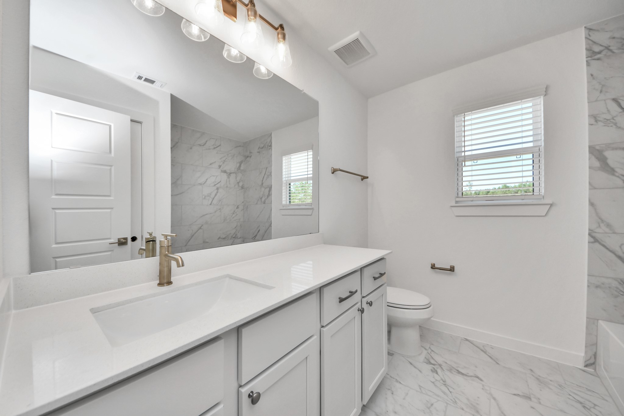 Secondary bath features tile flooring, bath/shower combo with tile surround, light stained wood cabinets, beautiful light countertop.