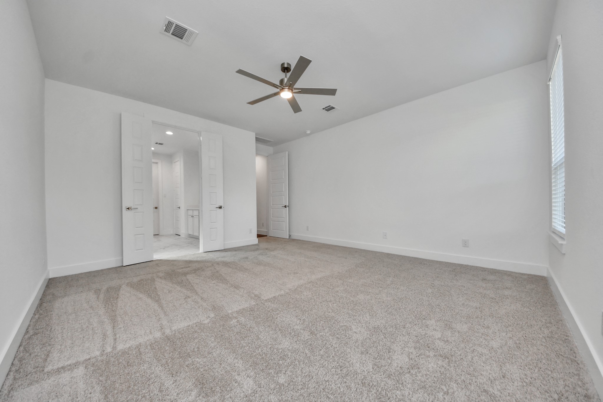 Escape and relax in the exquisite primary suite, a haven to unwind after a long day. The spacious room, located on first floor, boasts plush carpeting, soothing paint tones, high ceilings, and expansive windows adorned with privacy blinds.