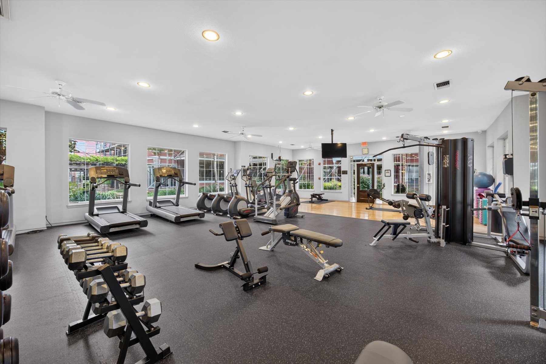 Building offers a fitness center equipped with modern cardio machines, free weights, and strength training equipment, surrounded by large windows for natural light.
