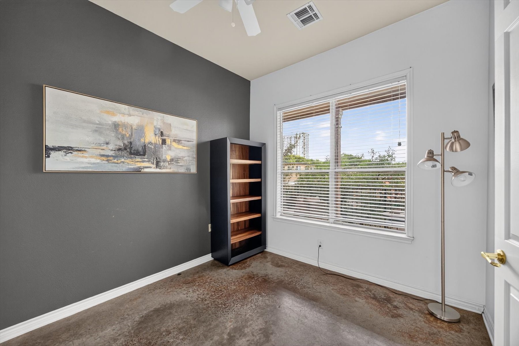 Additional room featuring a large window, modern gray accent wall, and polished concrete floors.   Ideal for a home office, nursery or second bedroom.