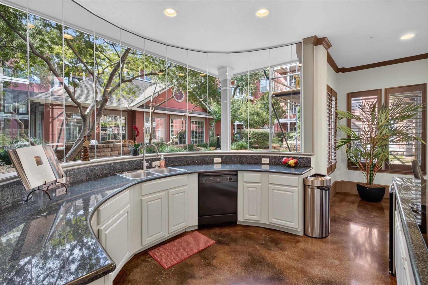 Clubhouse kitchen with panoramic windows offering serene garden views, featuring sleek granite countertops and modern appliances.