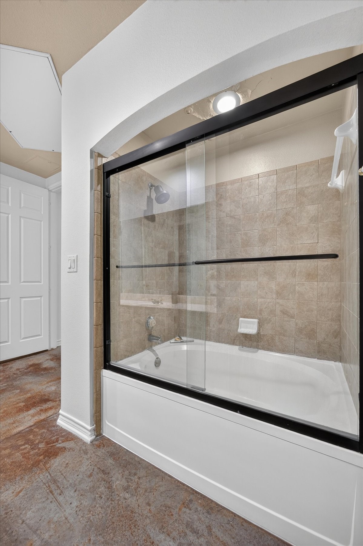 Elegant bathroom featuring a tiled shower-tub combination with sleek glass sliding doors, complemented by warm-toned tile walls and a polished concrete floor.