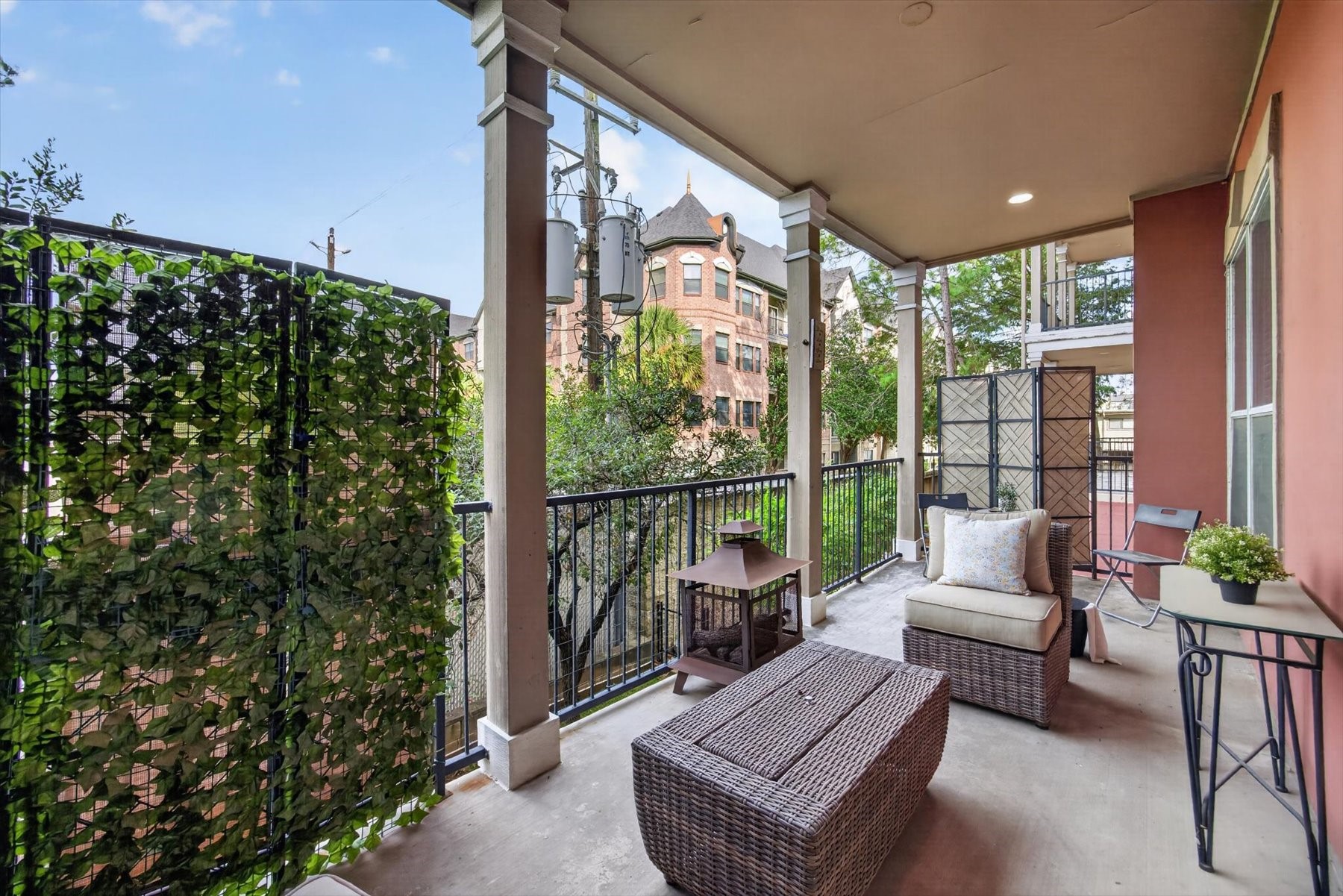 Spacious covered balcony with cozy seating, privacy screen, and charming views of the surrounding architecture and greenery, perfect for relaxation or entertaining.