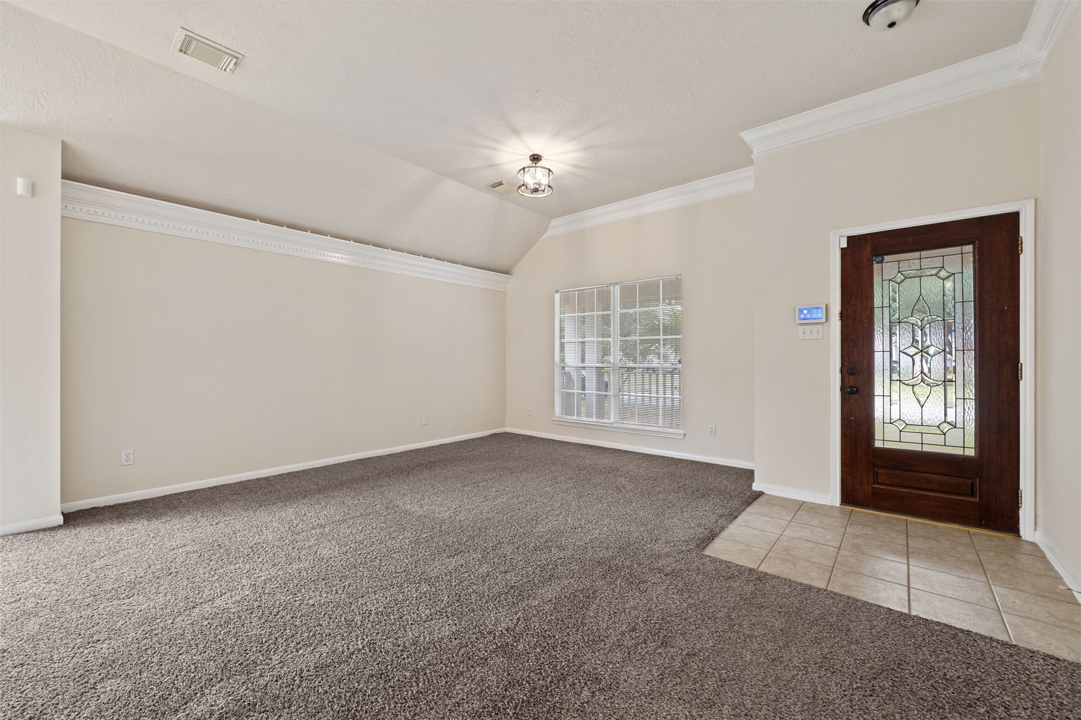 Focus on the living area with plush carpeting, elegant crown molding, and abundant natural light through a large window, complemented by a stylish wooden entry door with decorative glass.