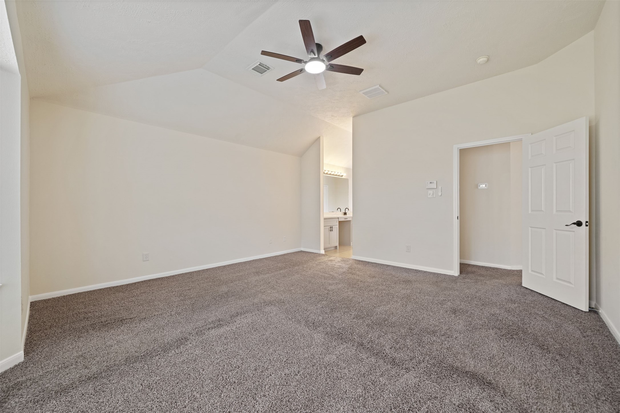 Plush carpeting, neutral walls, and a ceiling fan, featuring an open entrance to a well-lit en-suite bathroom for added convenience.