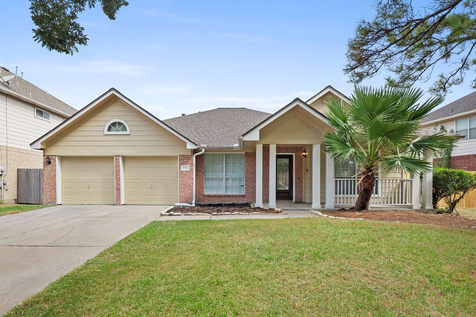 Charming single-story home with a New Roof (June 2026), welcoming front porch, dual garage doors, and a well-maintained lawn, accented by a mature palm tree.