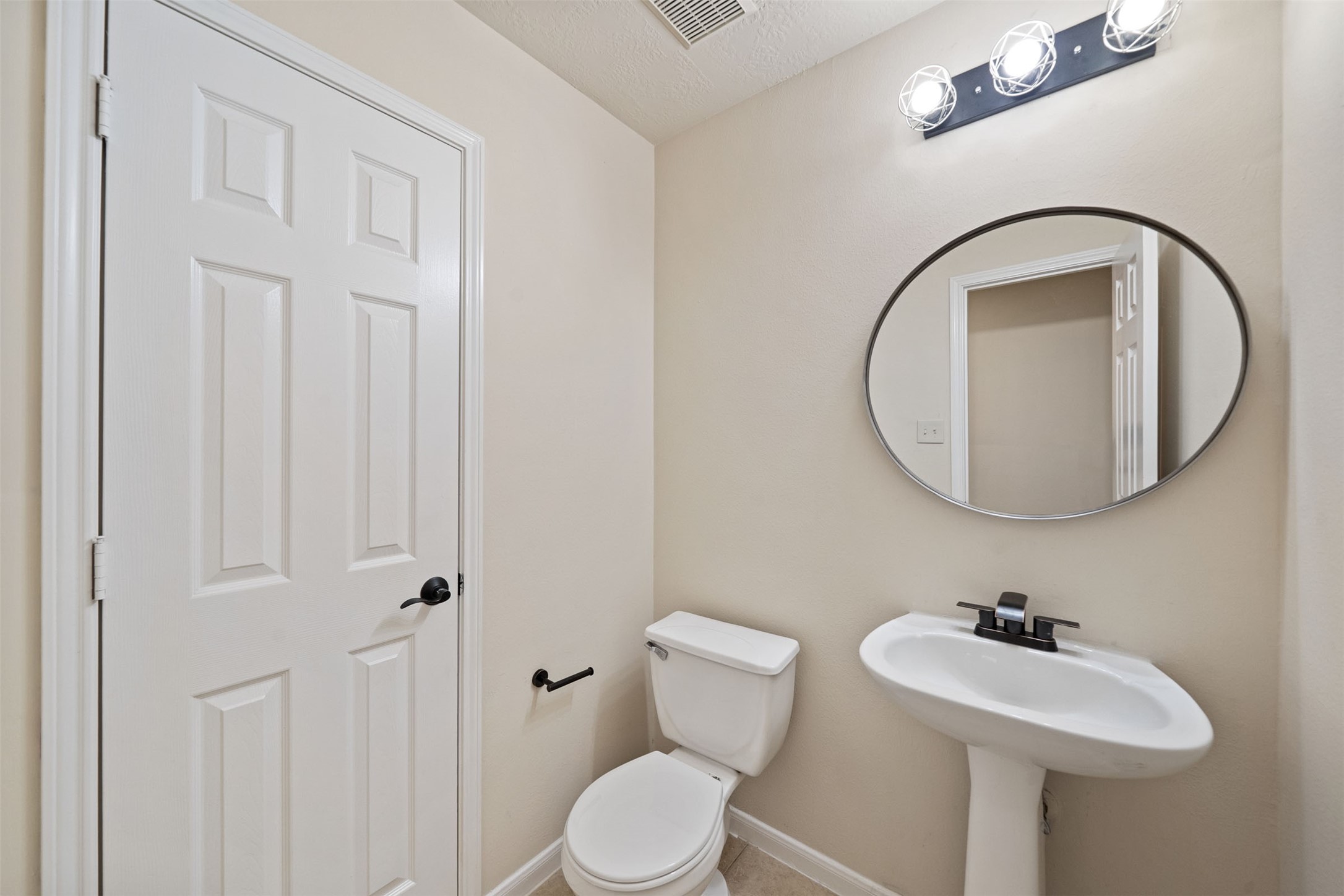 Charming powder room with a sleek pedestal sink, modern mirror, and bright lighting, offering a clean and functional space.
