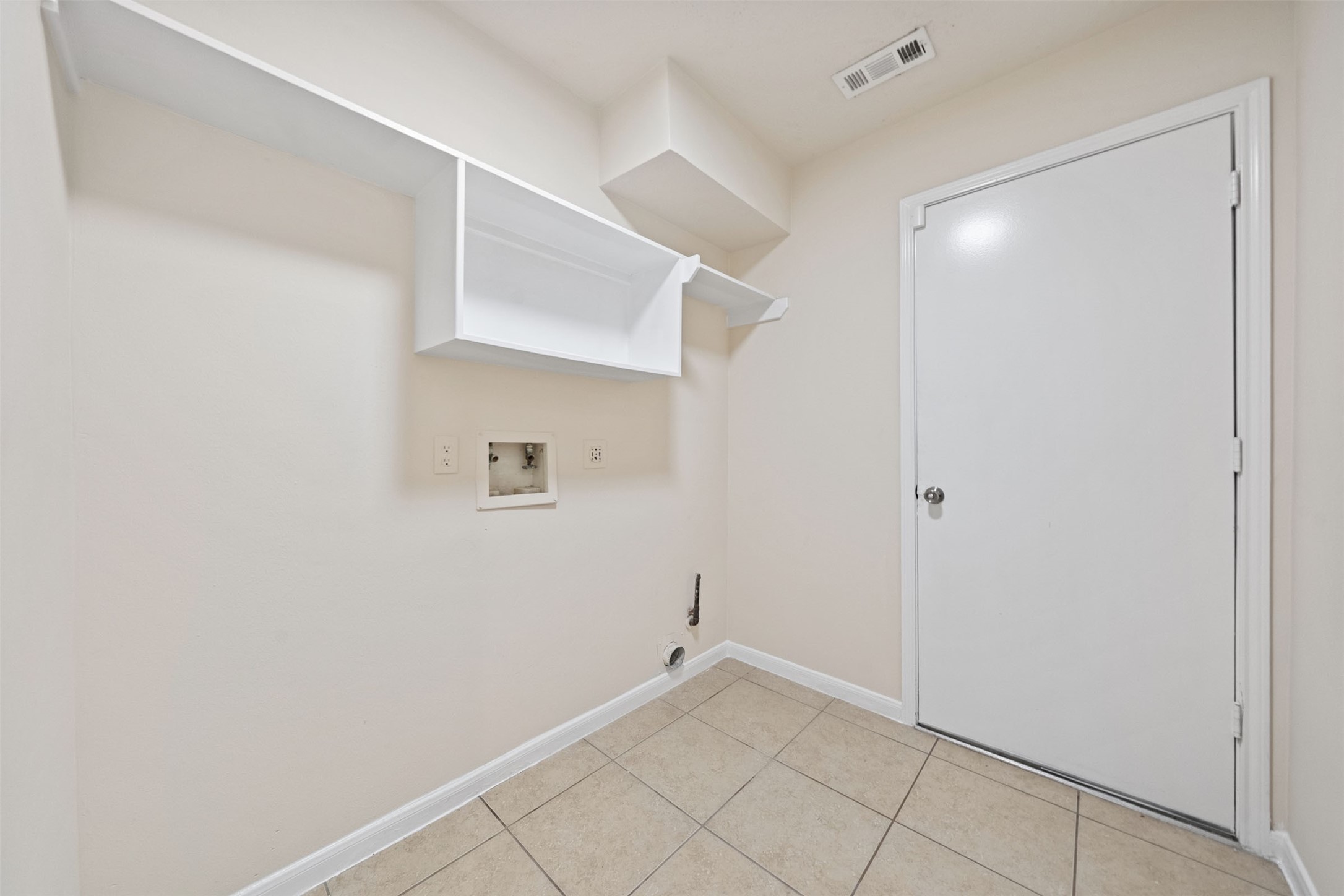 Laundry room with tiled floors, wall shelving, and hookups for a washer and dryer, providing functionality and storage.
