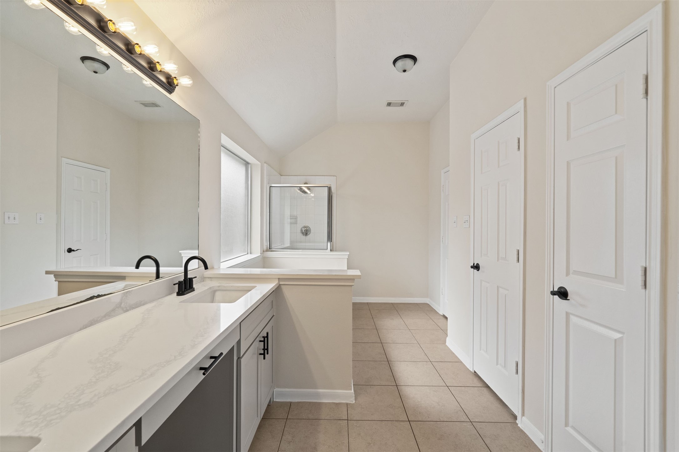 Renovated bathroom featuring a dual-sink vanity with modern fixtures, ample mirror space, and a large shower, all complemented by elegant tile flooring.