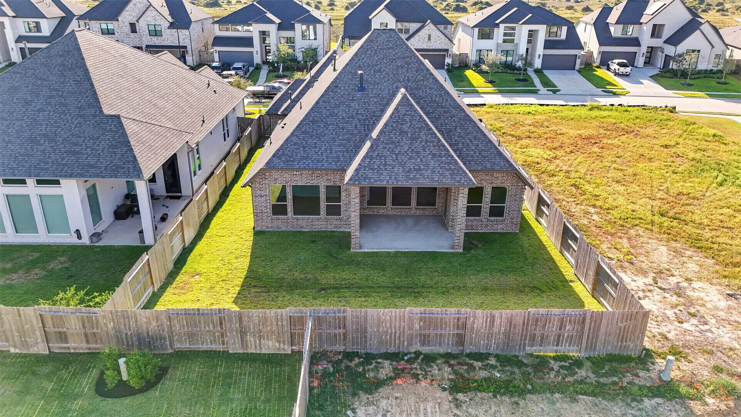Aerial Rear Exterior & Backyard: Stunning aerial perspective showcasing the home's beautiful brick exterior, expansive covered patio, and spacious, fully fenced backyardoffering an inviting setting for outdoor living and entertaining.