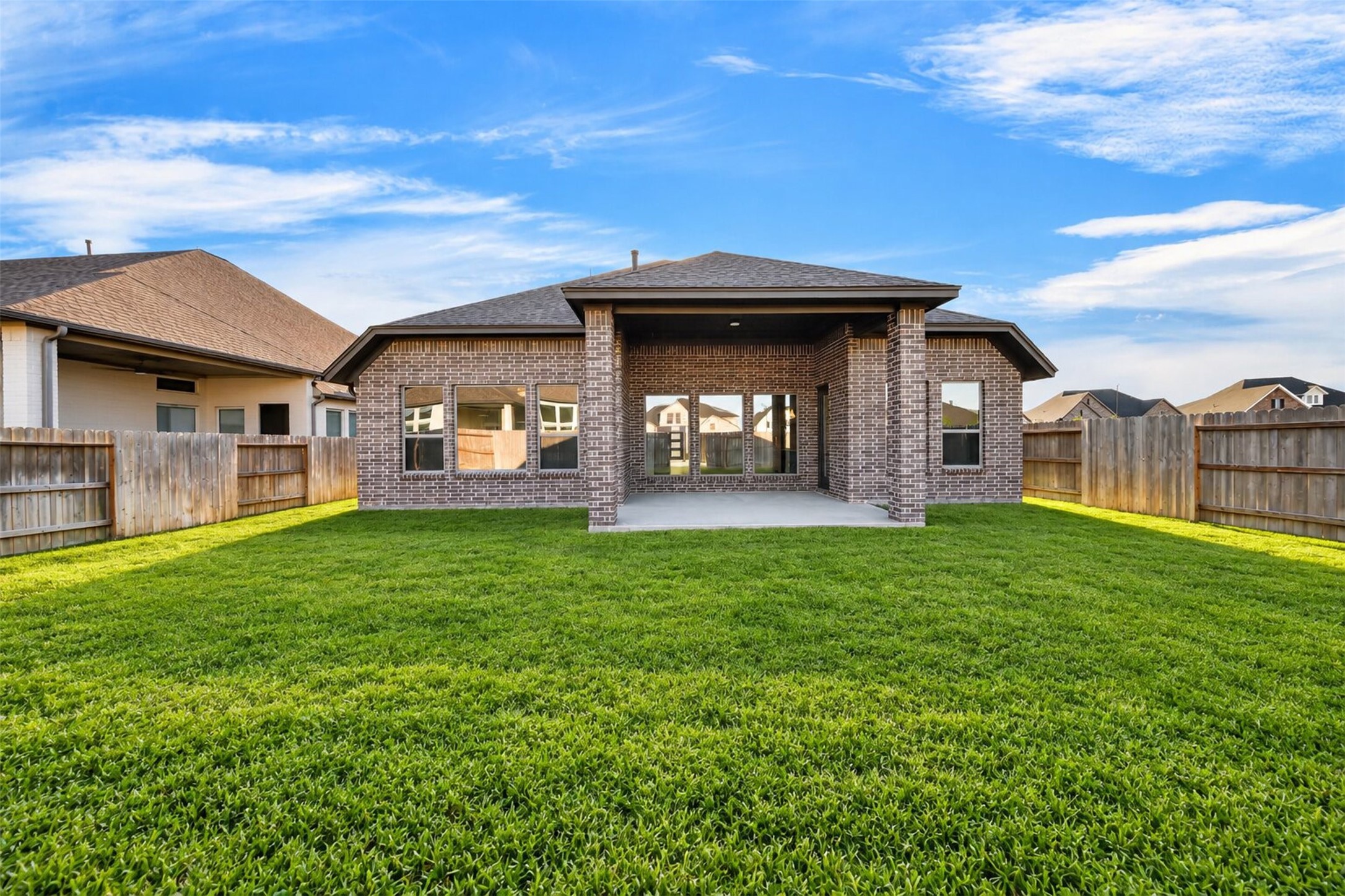 Rear Exterior & Covered Patio: Beautiful brick exterior overlooking a spacious, fully fenced backyard with lush green lawn and a generous covered patio designed for outdoor living and entertaining.