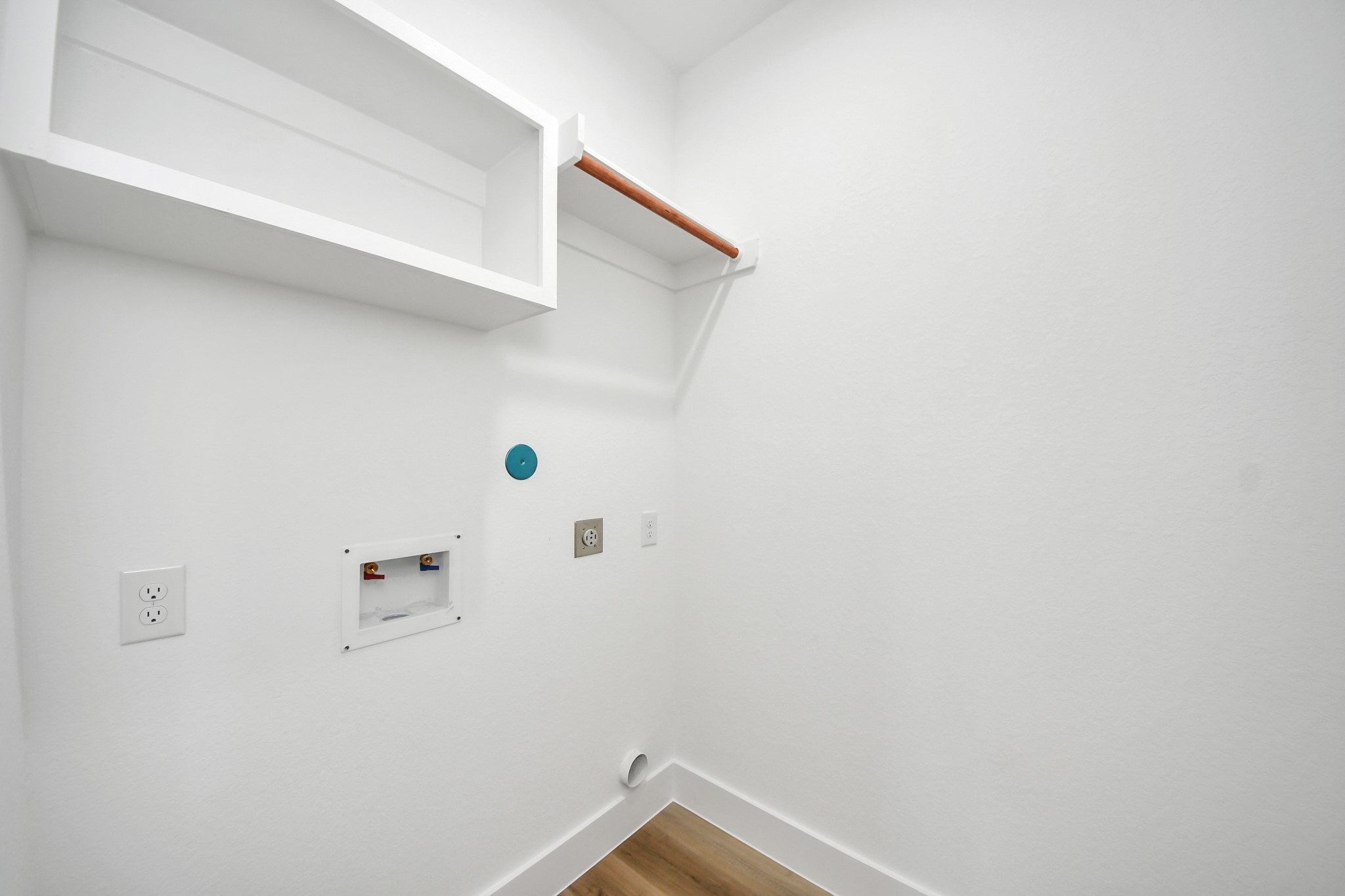 Laundry area equipped with hookups, a shelf for storage, and a hanging rod, offering convenience and functionality.