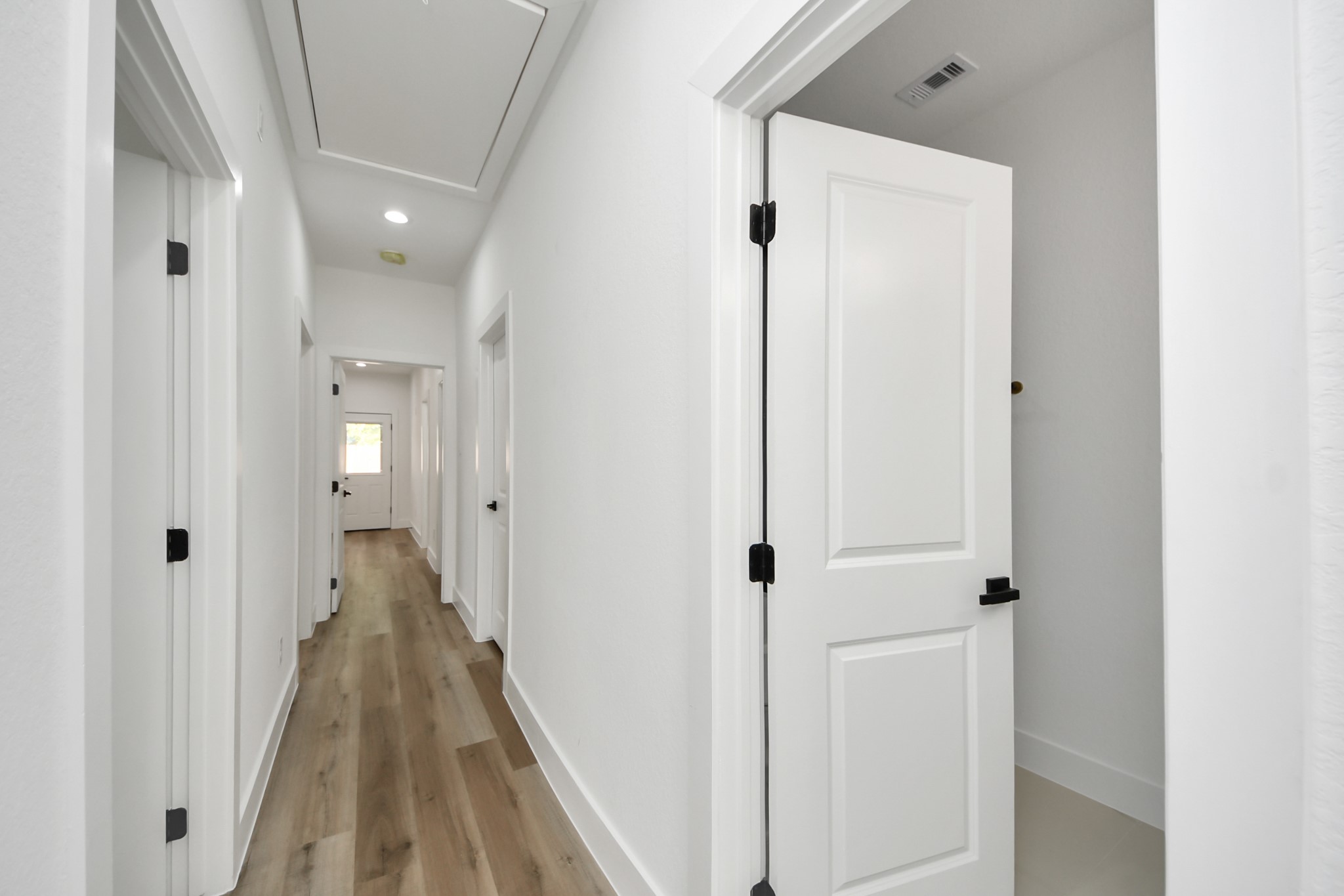Bright and inviting hallway with sleek wood flooring and modern white doors, leading to various rooms in the home.