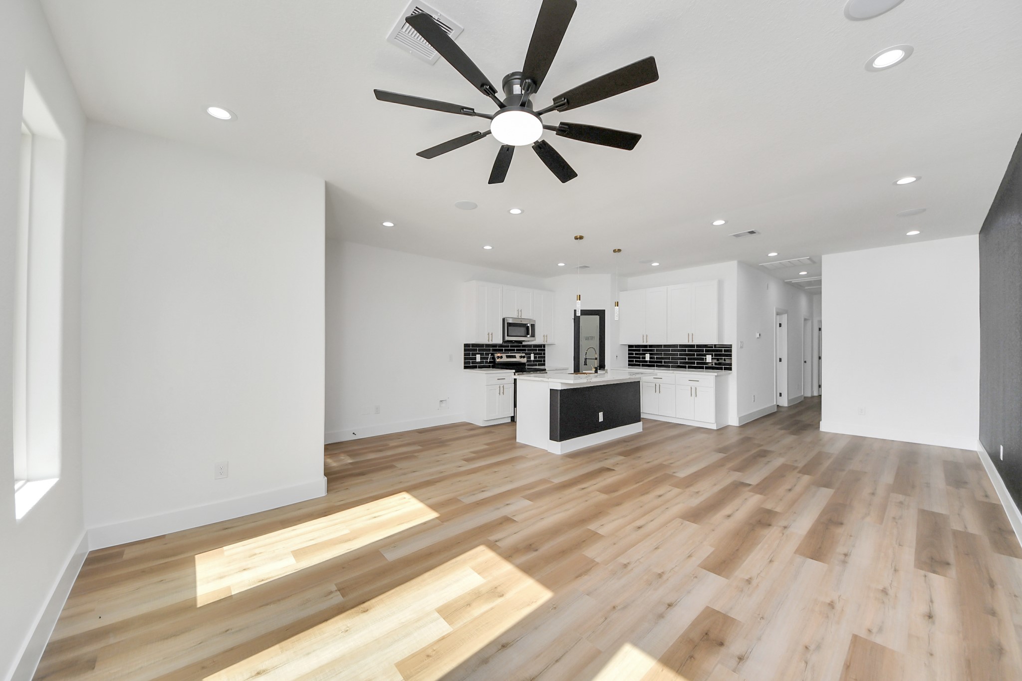 Spacious open-concept living area featuring sleek hardwood floors, a modern kitchen with stylish black backsplash, and ample natural light.