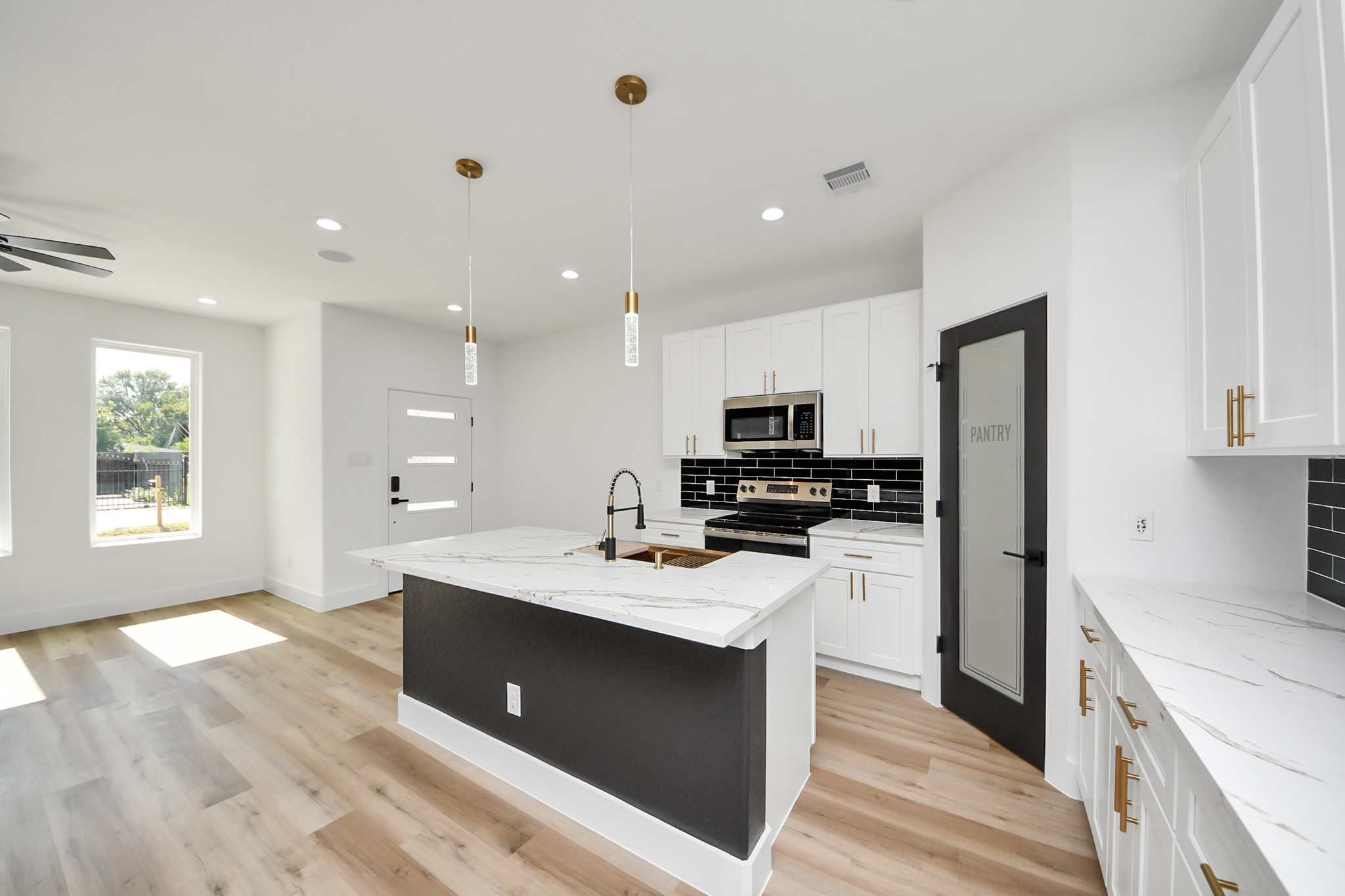 Modern kitchen with sleek black and white cabinetry, marble countertops, and stainless steel appliances. Bright, open layout with stylish pendant lighting and a walk-in pantry.