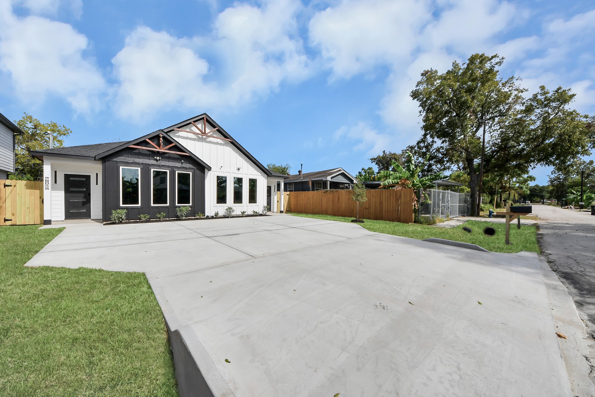 Charming modern home with a striking black and white exterior, expansive windows, and a spacious driveway, nestled in a tranquil neighborhood.