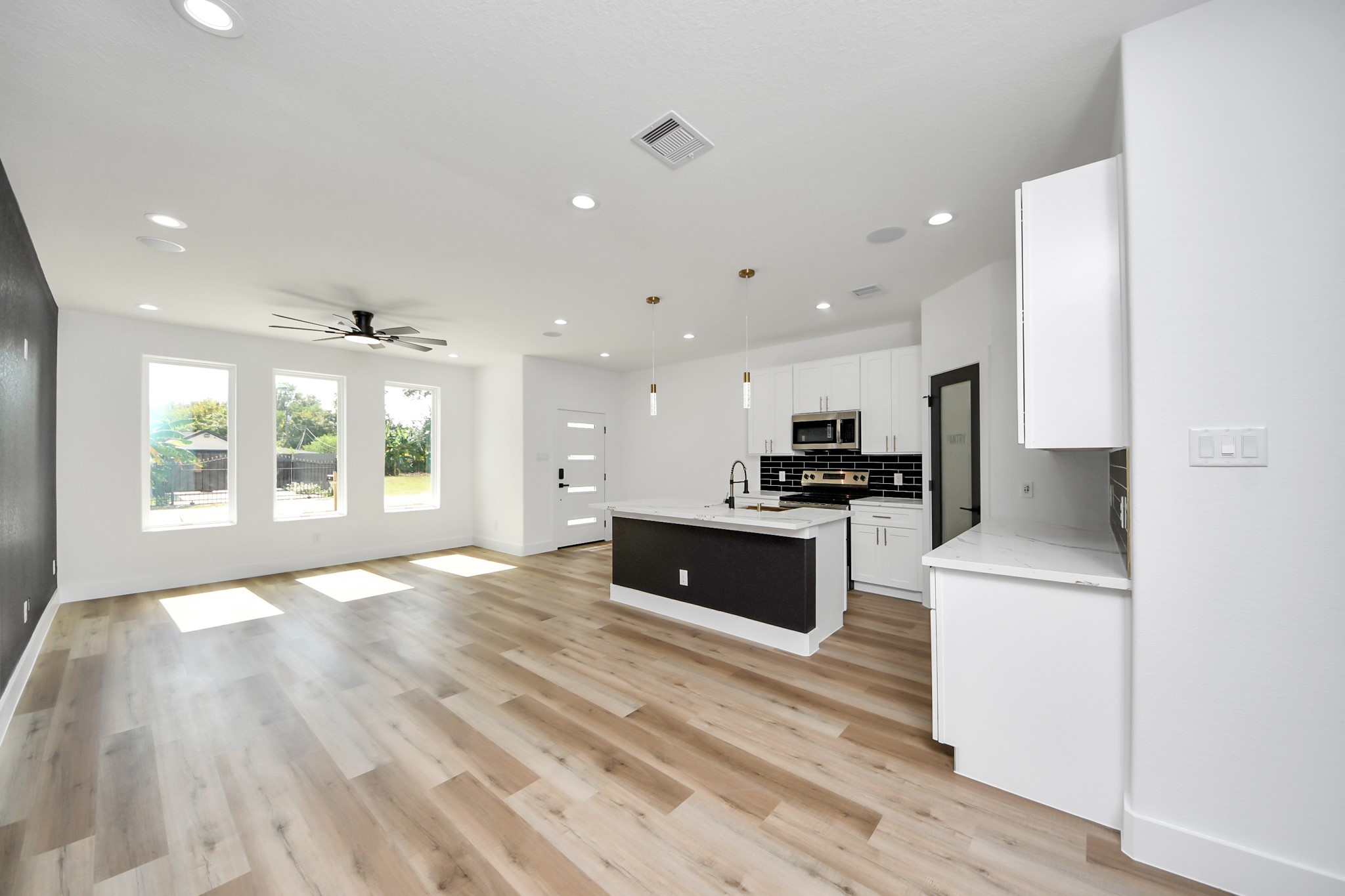Spacious open-concept living area with abundant natural light, featuring sleek wood flooring, a modern kitchen with a central island, and stylish black and white cabinetry.