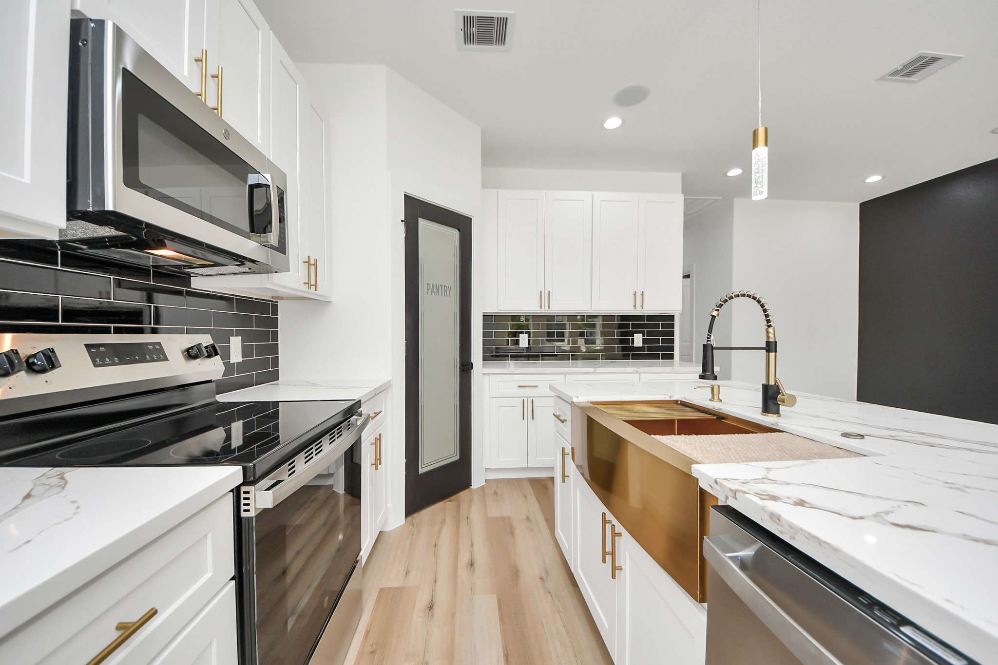 Modern kitchen featuring sleek white cabinetry, stainless steel appliances, and elegant marble countertops. The black subway tile backsplash adds a touch of sophistication, complemented by a contemporary gold faucet and stylish pantry door.