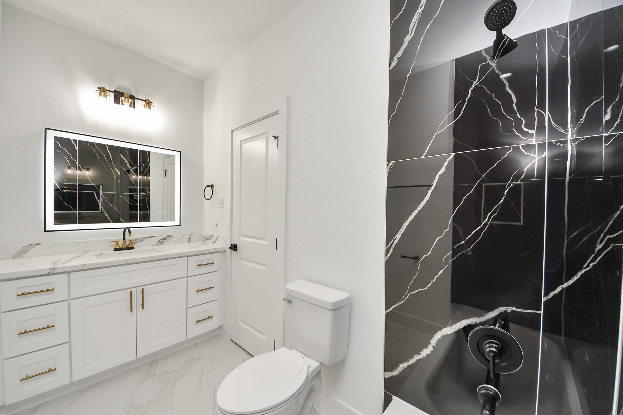 Elegant bathroom featuring a striking black marble shower with white veining, complemented by a sleek vanity with gold fixtures and ample storage.