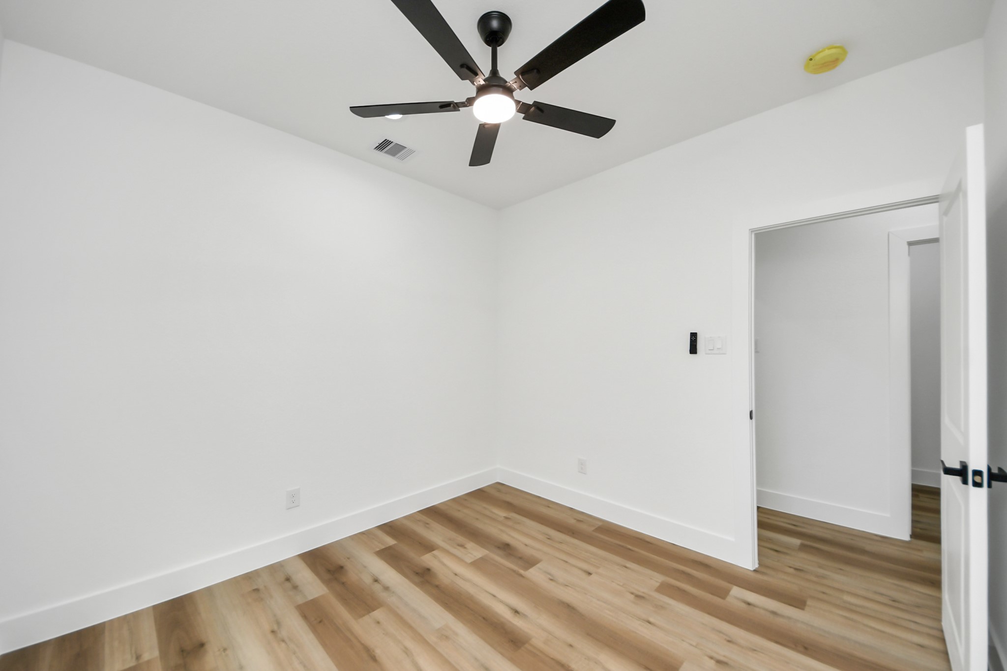 Bright and inviting room with sleek hardwood floors, a modern ceiling fan, and crisp white walls, perfect for a cozy bedroom or home office.