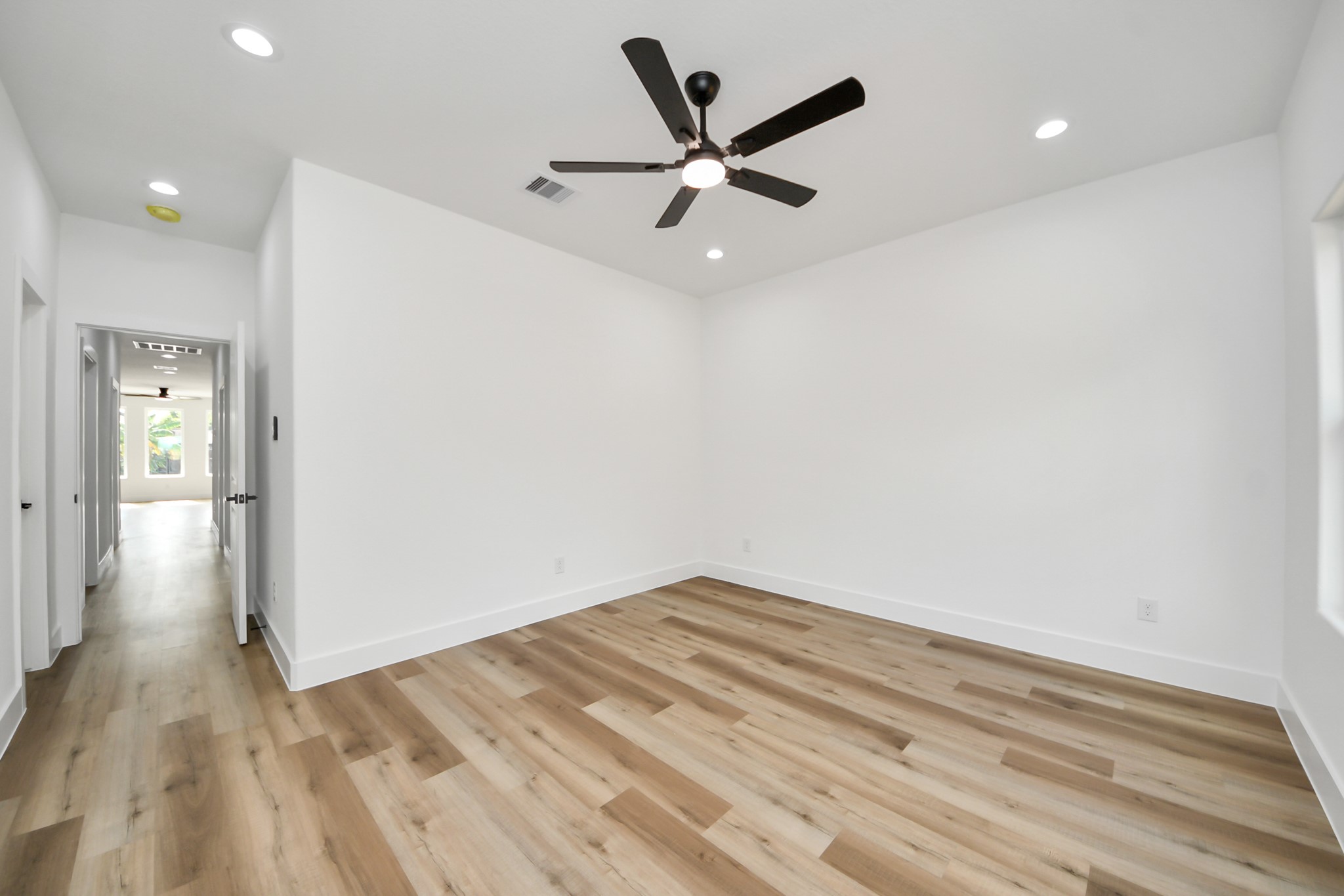 Spacious and bright room with sleek hardwood floors and a modern ceiling fan, offering a versatile layout ideal for various uses.